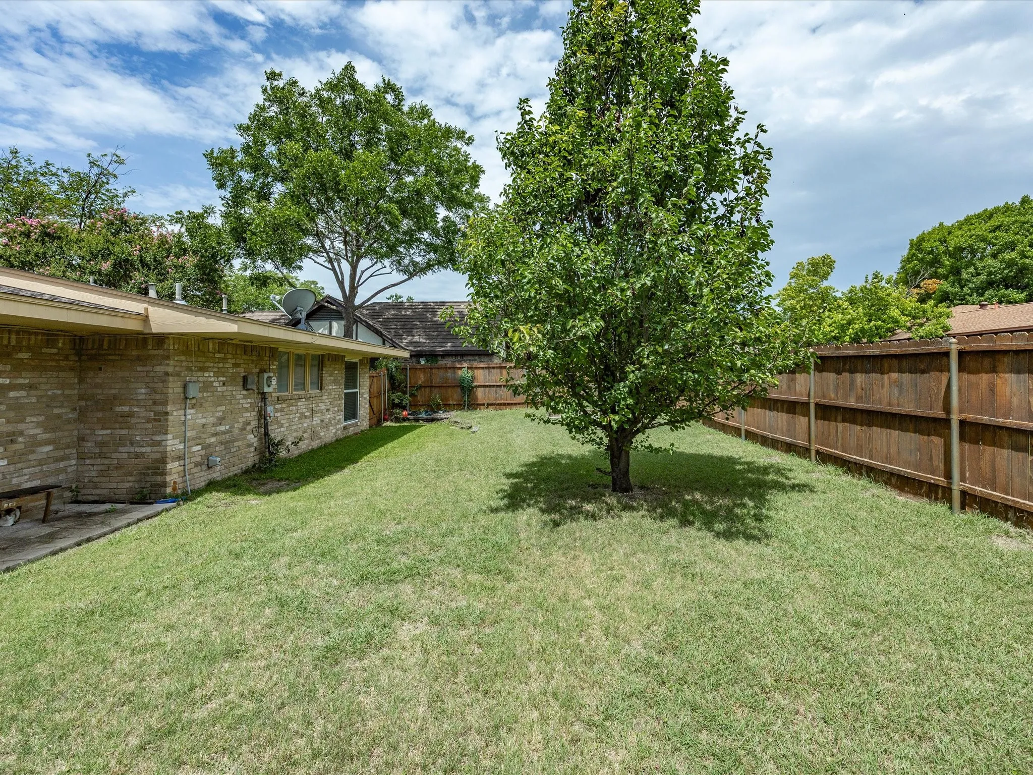 Spacious green lawn with mature shade trees, full privacy fencing, and brick exterior