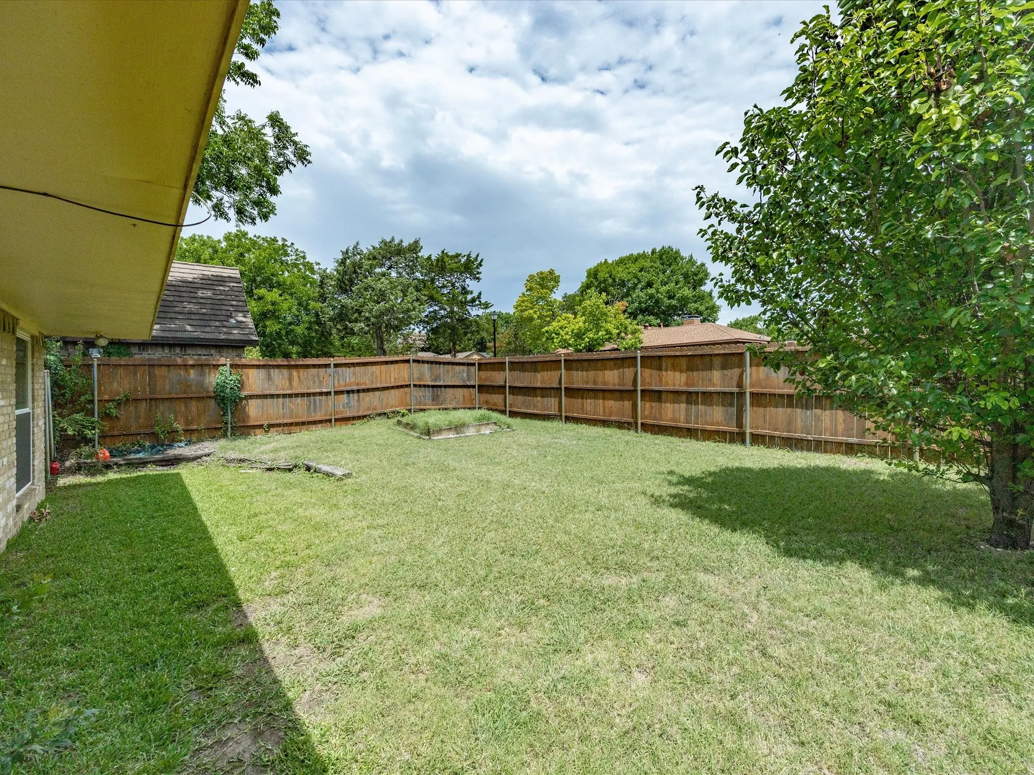 Expansive backyard featuring a large grass lawn, perimeter wood fencing, mature trees, and a raised garden bed