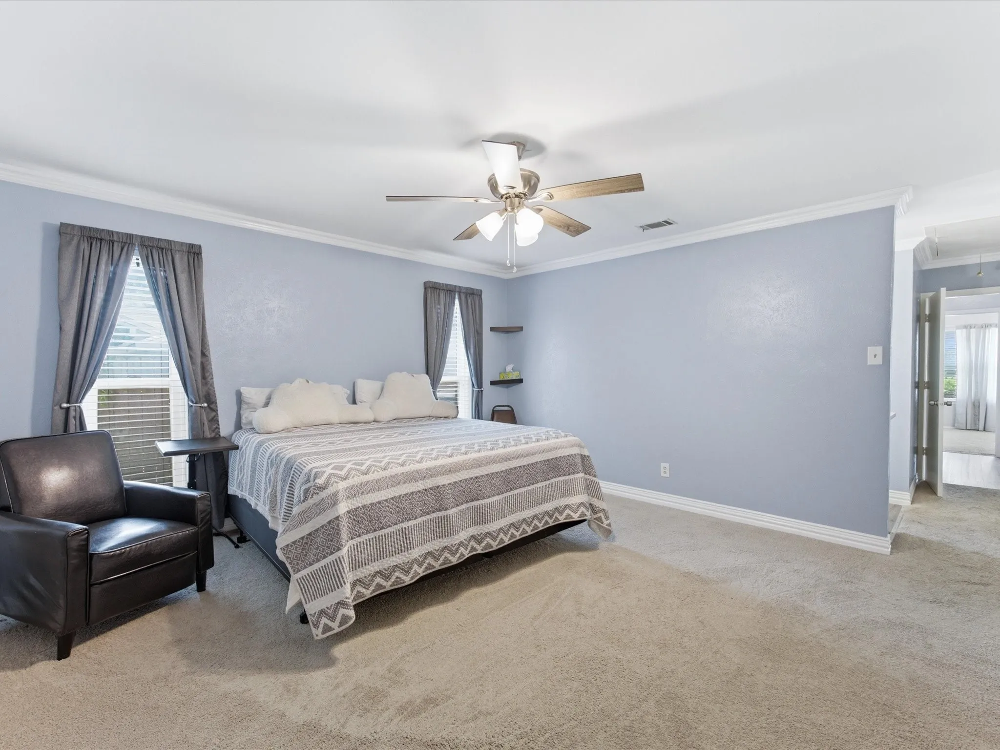 Spacious room featuring light blue walls, plush carpet, white crown molding, and a ceiling fan