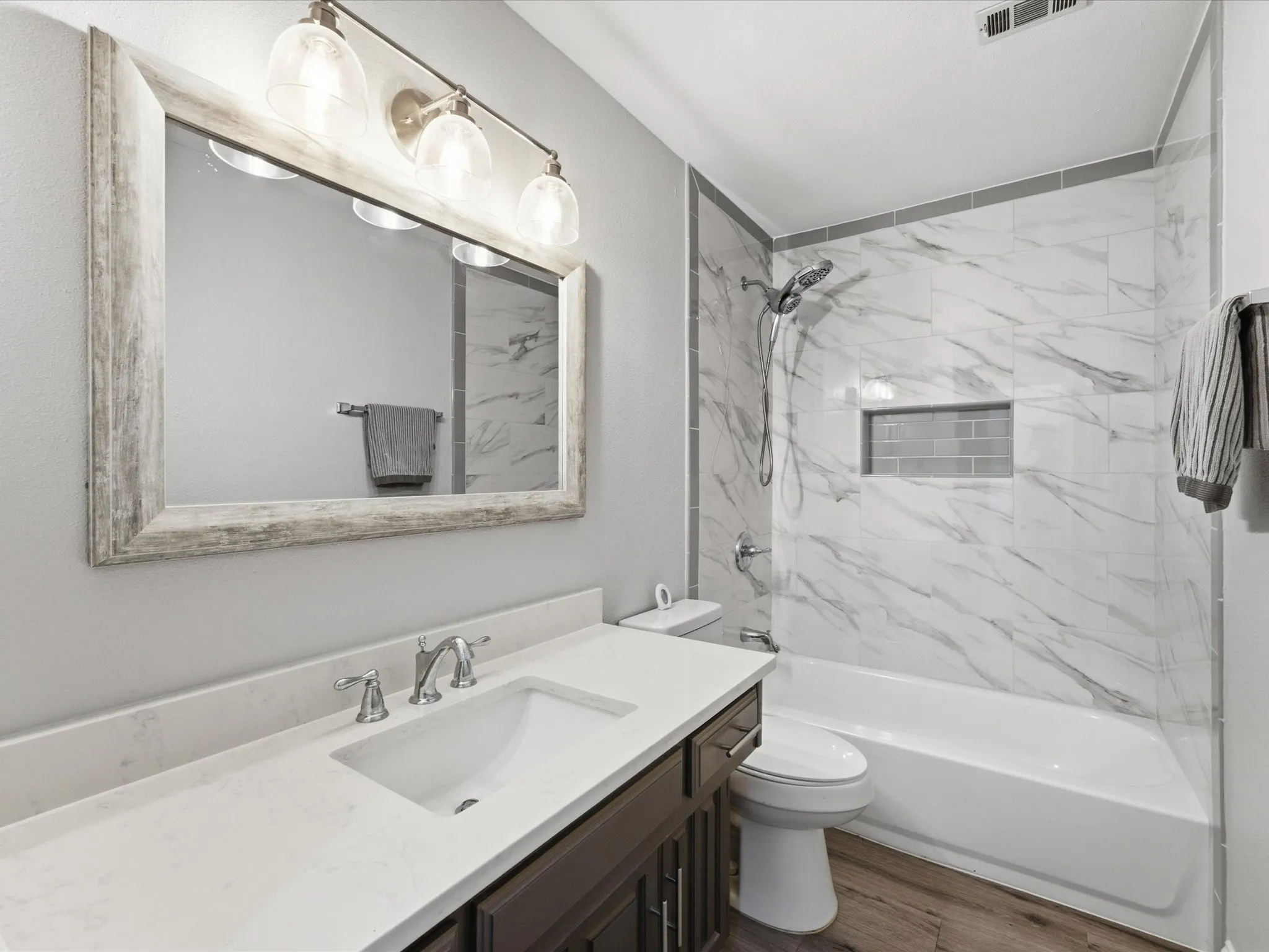 Bathroom featuring a vanity with an integrated sink, polished chrome faucet, and a large framed mirror with overhead lighting