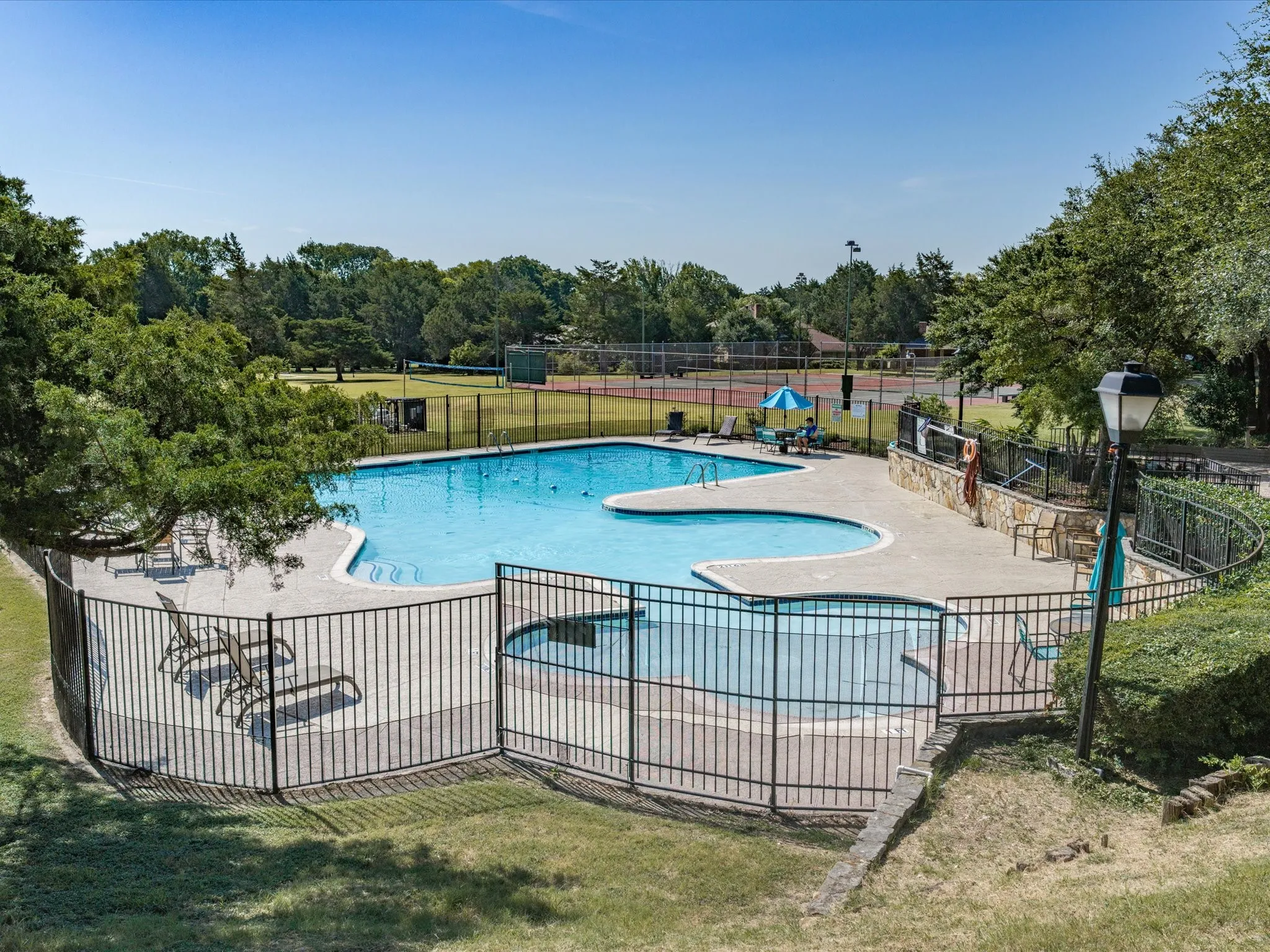 Multi-level swimming pool with integrated spa, surrounded by a paved deck and black metal fencing