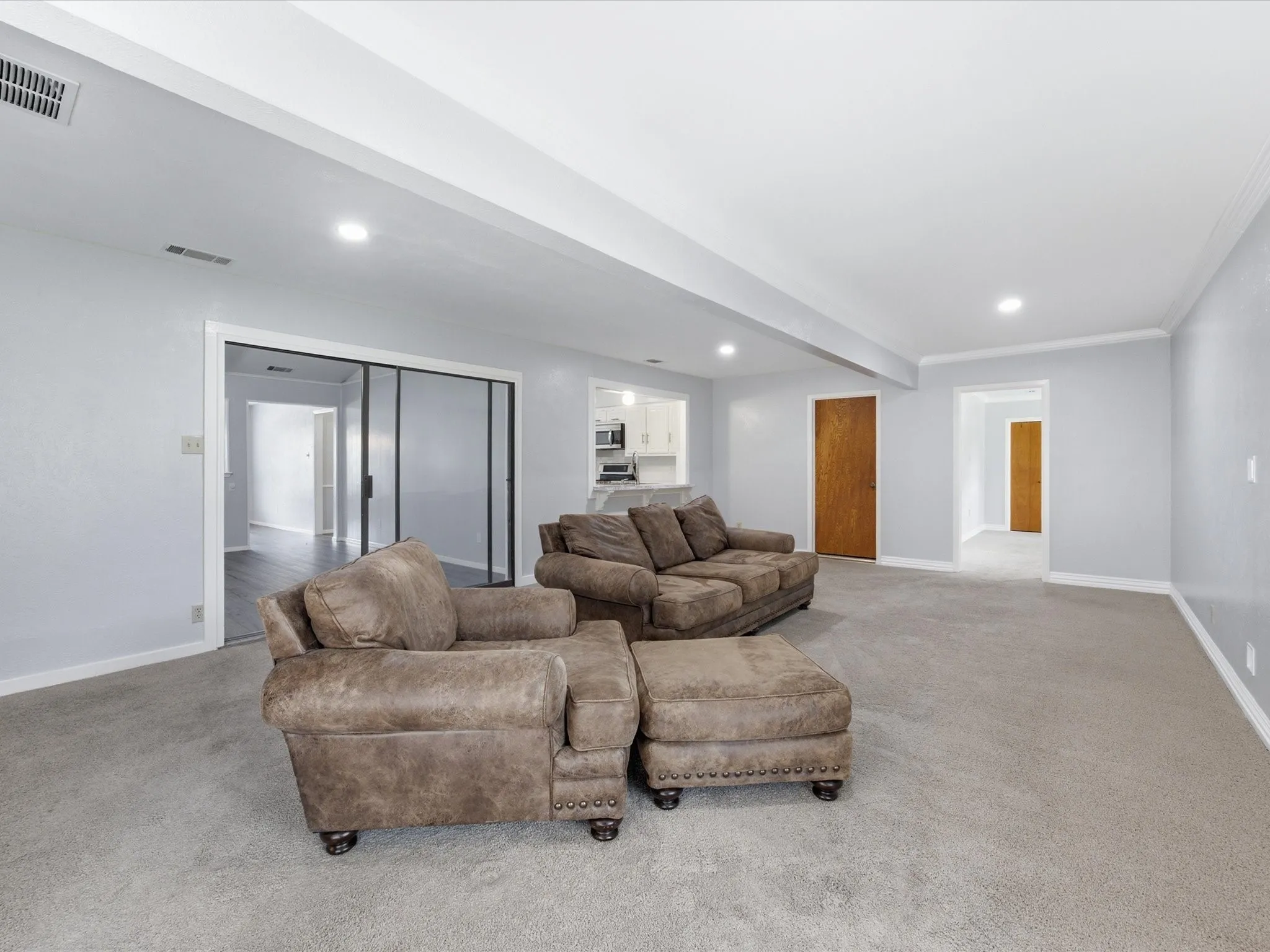 Spacious living area featuring light gray carpeting and walls, white crown molding, and recessed lighting