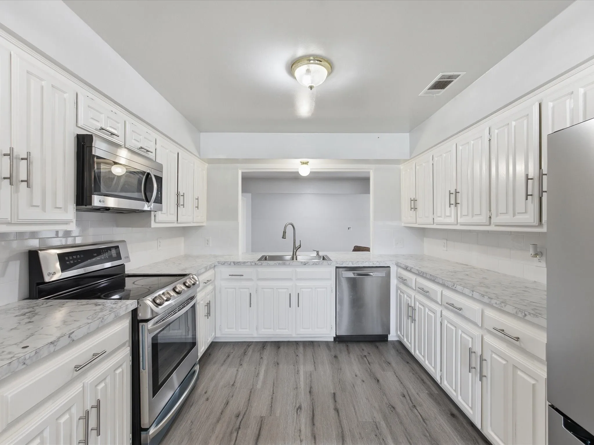 Galley kitchen featuring white cabinetry, light countertops, wood-finish flooring, stainless steel appliances, and a subway tile backsplash