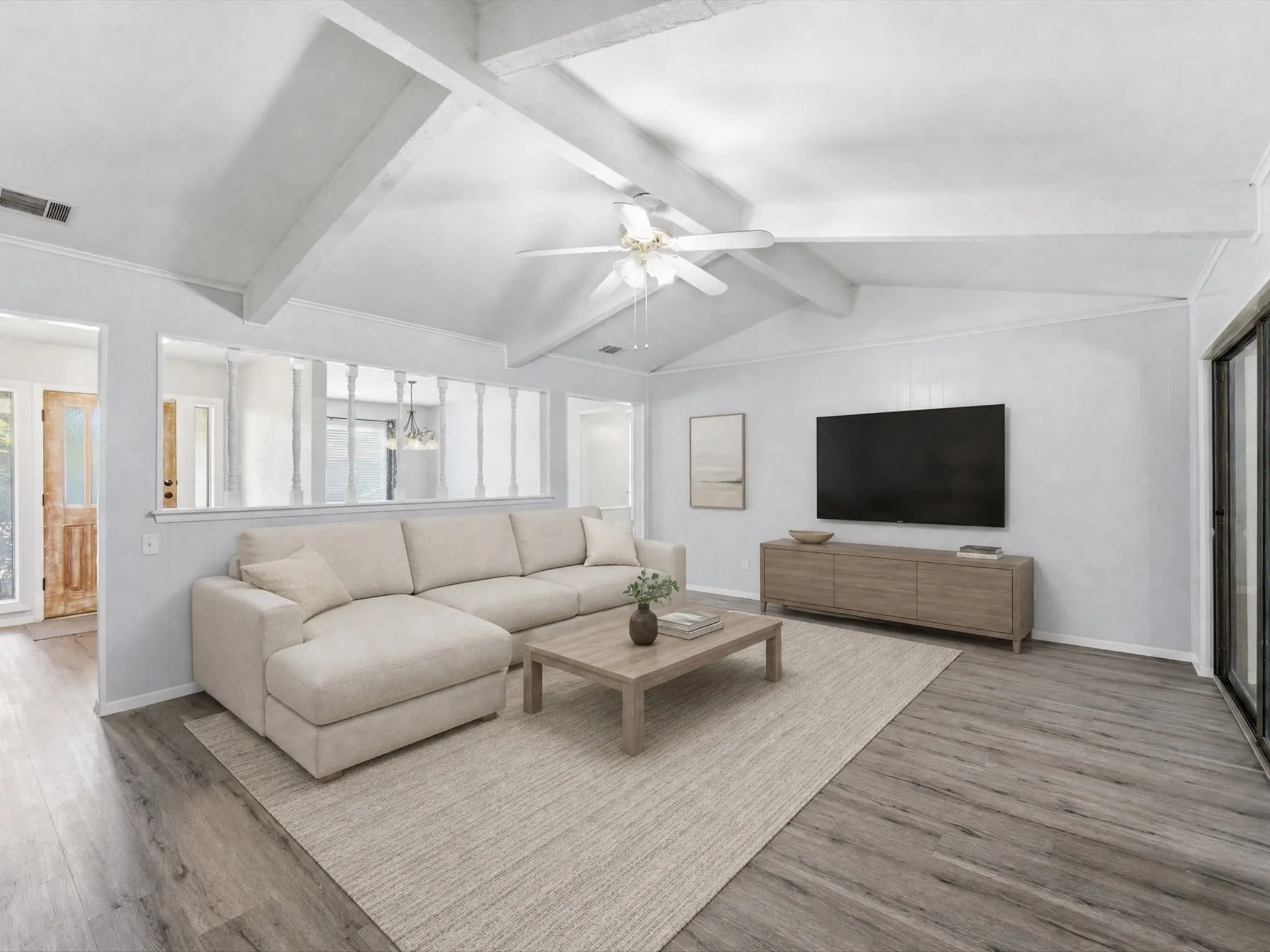 Virtually staged Living Room with vaulted ceiling with exposed beams, wood-finish flooring, half-wall with decorative spindles, overhead ceiling fan, and a sliding glass door