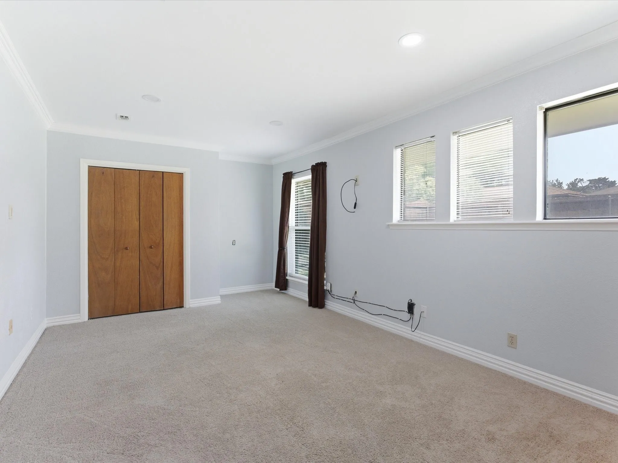Carpeted bedroom featuring a double bifold door closet with wood-finish panels, multiple windows with blinds, recessed lighting, and crown molding