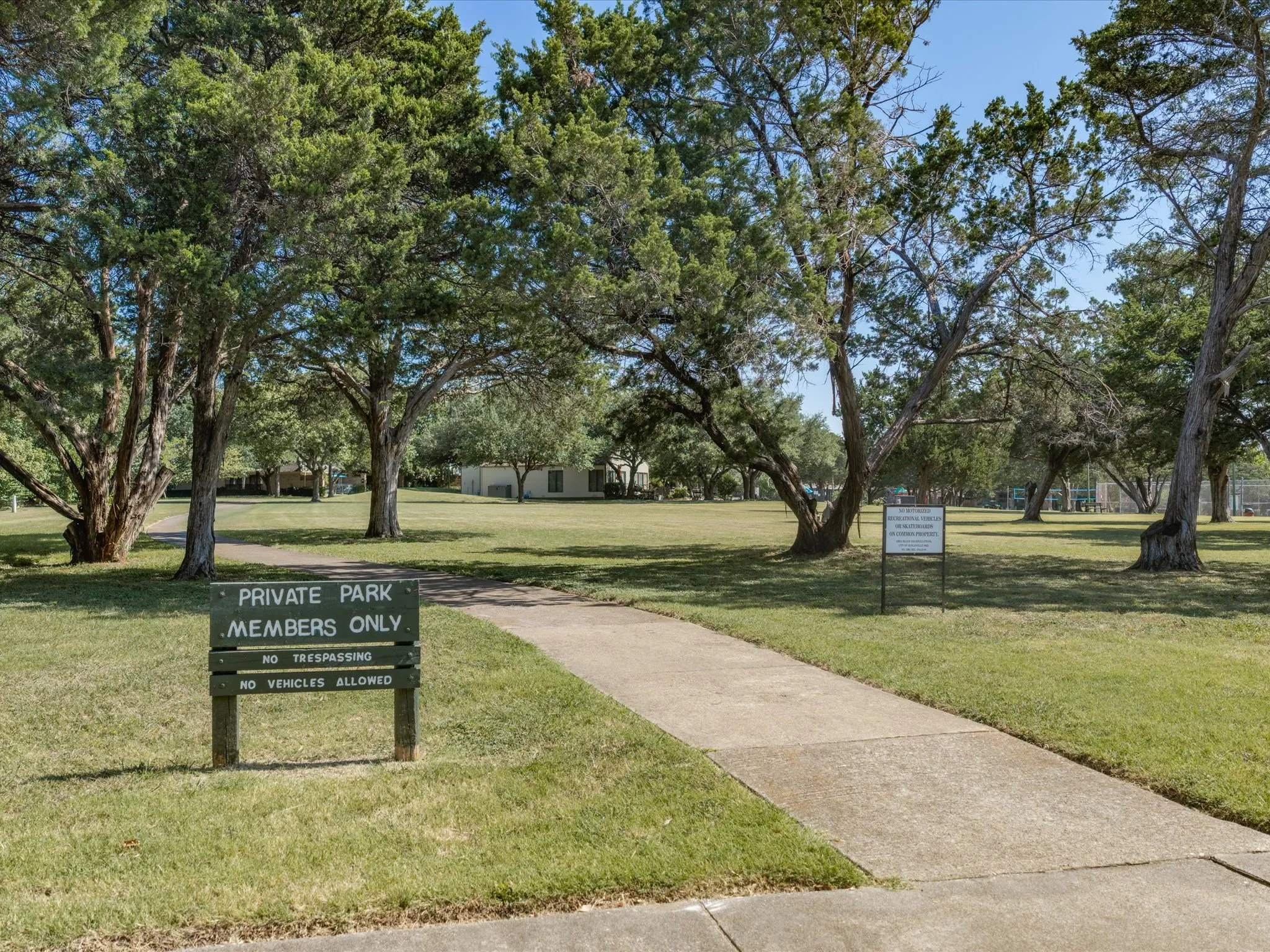 Private park entrance featuring a concrete pathway, mature trees, and a manicured lawn
