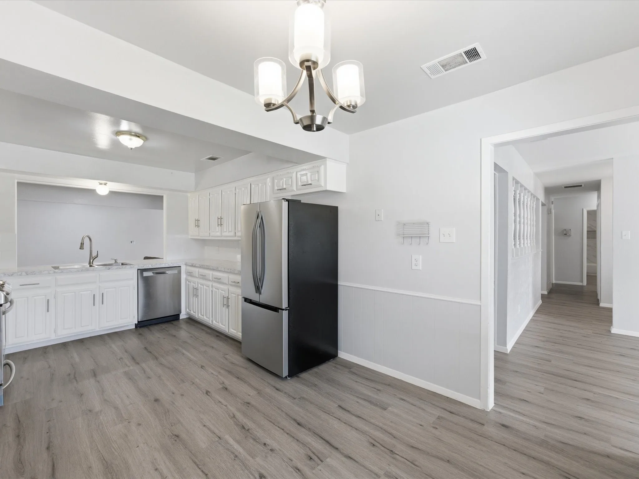 Kitchen featuring wood-finish flooring, white cabinetry, stainless steel appliances, and a pass-through window
