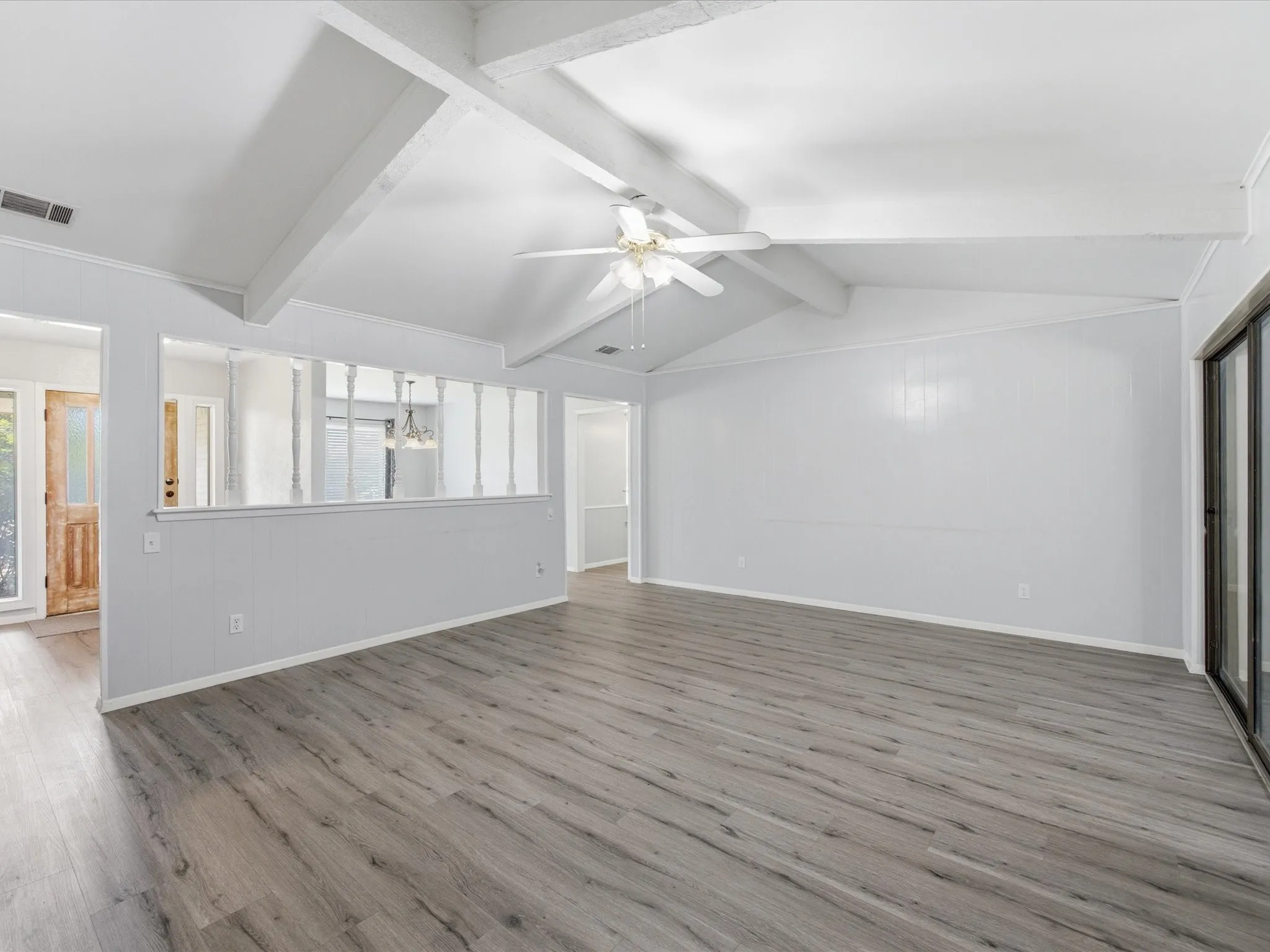 Living Room with vaulted ceiling with exposed beams, wood-finish flooring, half-wall with decorative spindles, overhead ceiling fan, and a sliding glass door