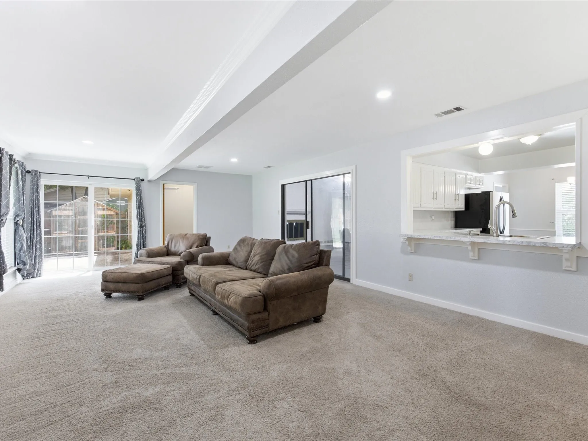 Spacious living area featuring light-colored carpeting, recessed lighting, and a pass-through window with a breakfast bar