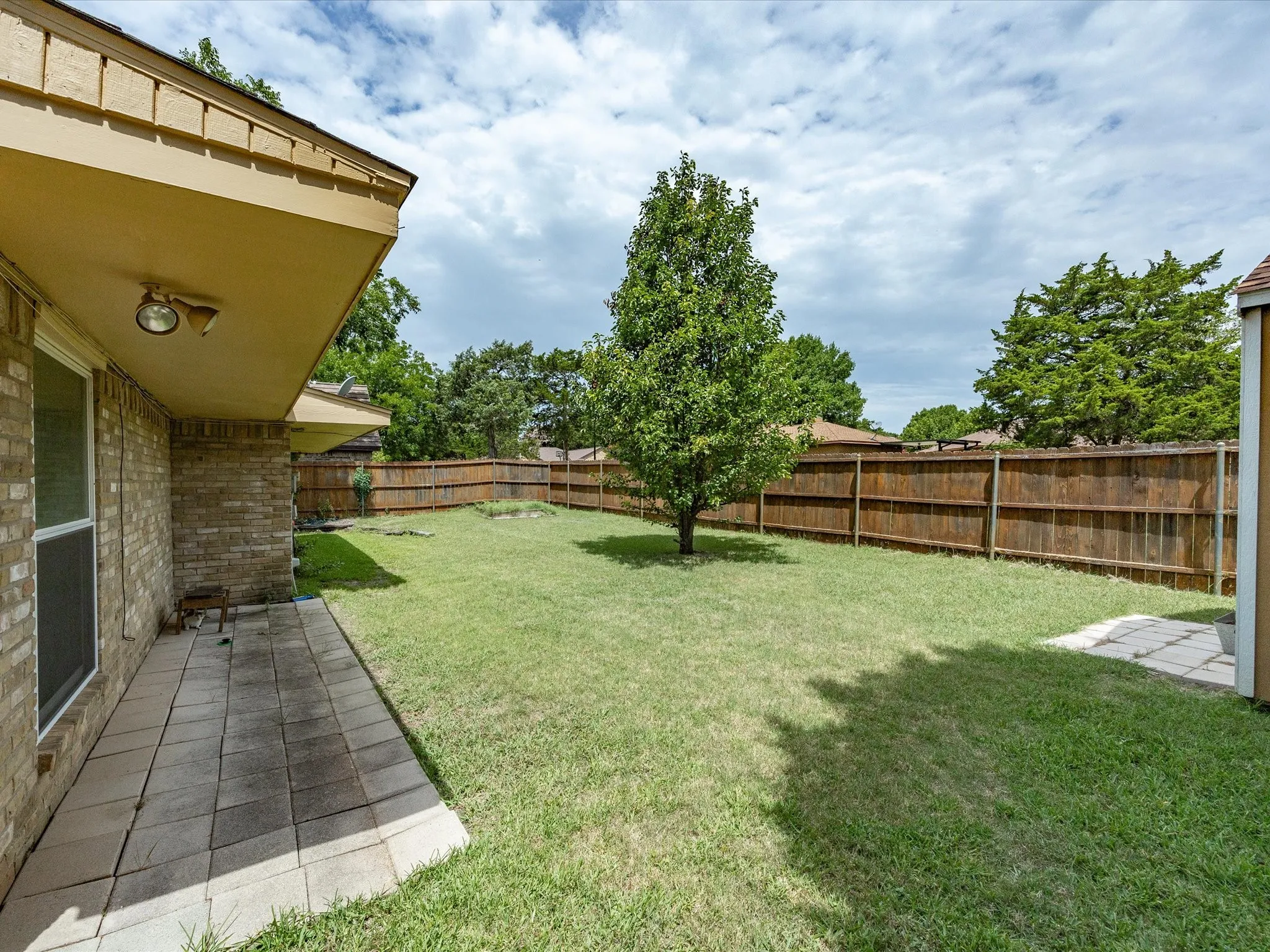 Spacious backyard featuring a privacy fence, mature tree, and a paved patio area