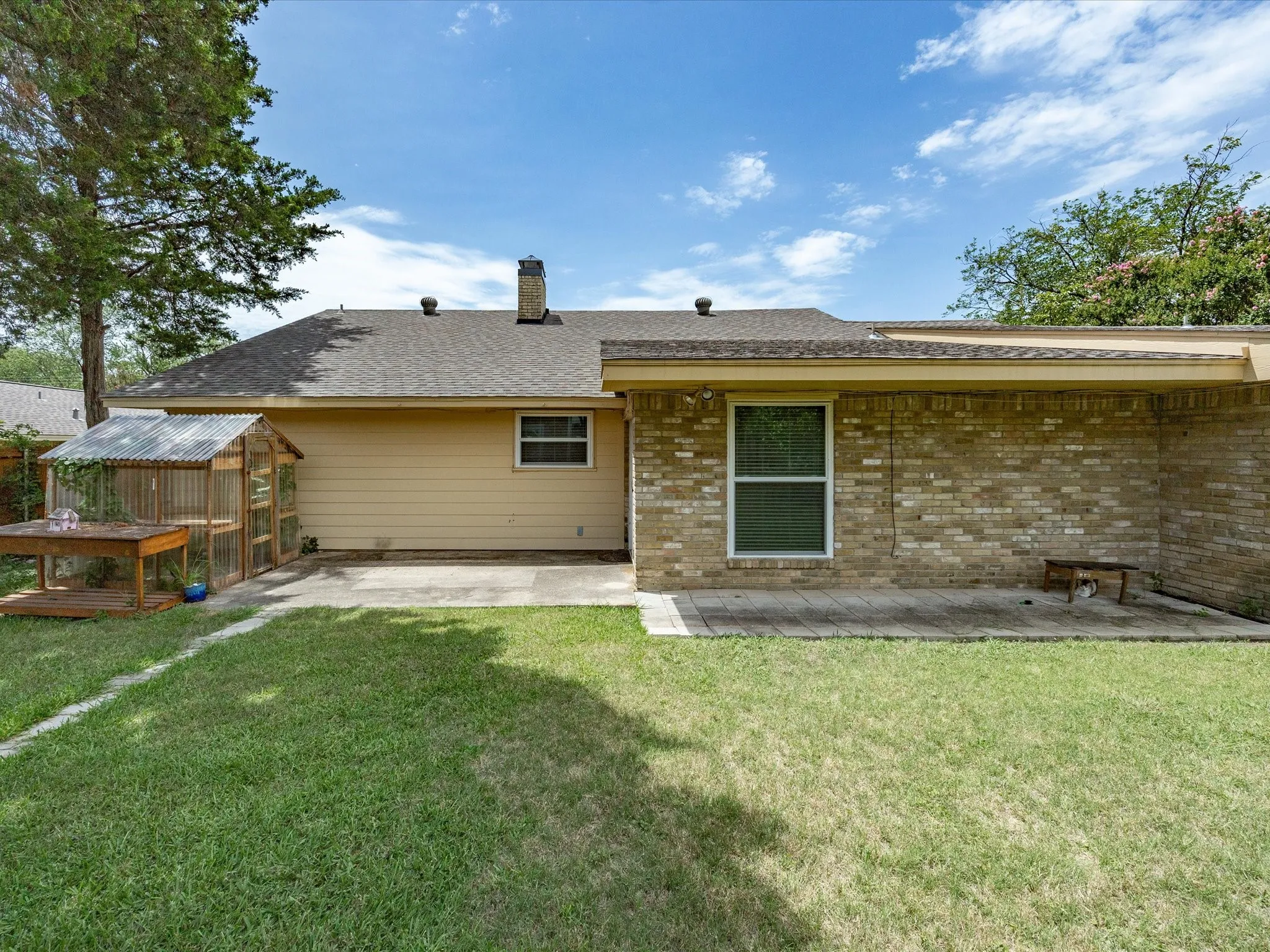 Expansive backyard featuring a manicured lawn, a paved patio area, and a custom-built outdoor structure with a corrugated metal roof