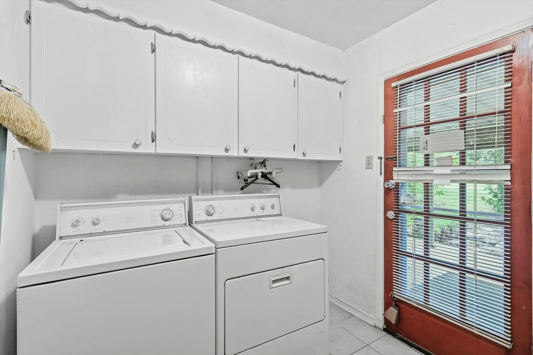 Dedicated utility area featuring white upper cabinetry, tiled flooring, and a red-toned exterior door with integrated blinds