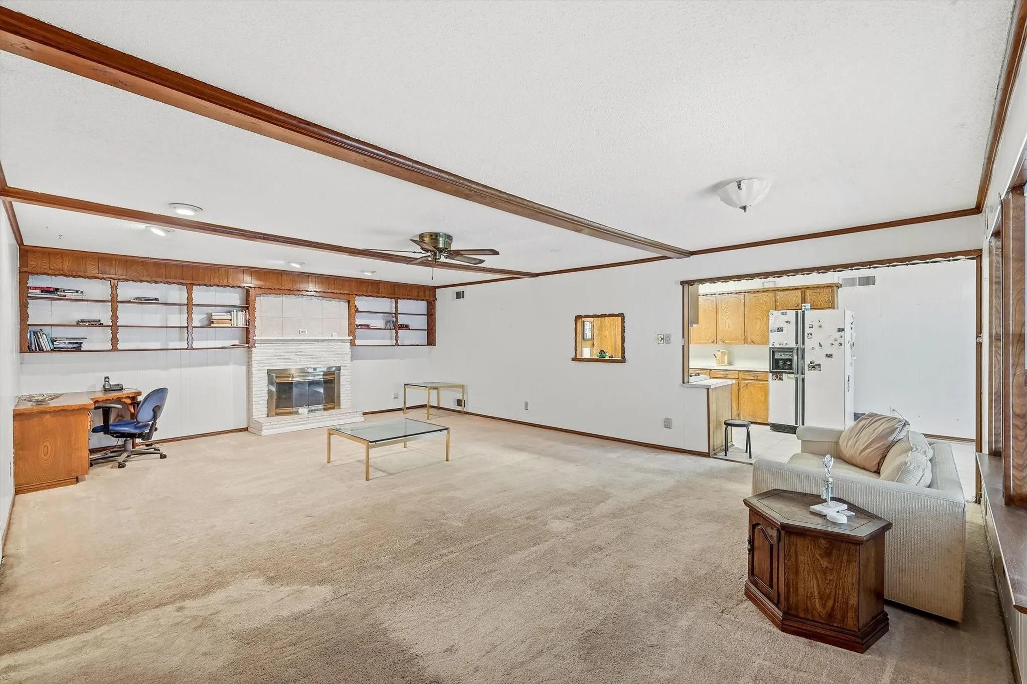 Spacious living area featuring exposed wood beams, a white brick fireplace, and built-in shelving