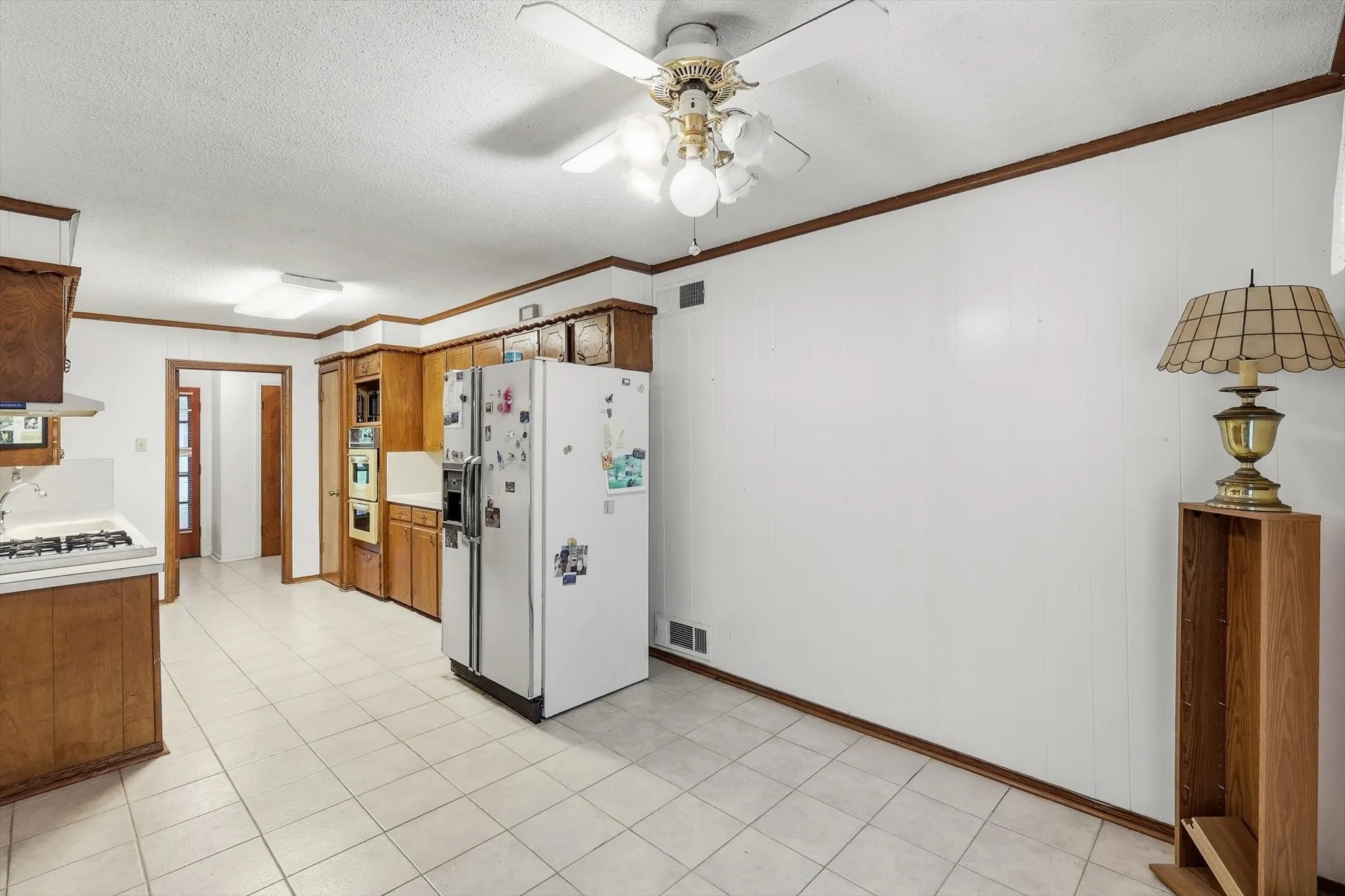 Kitchen featuring wood cabinetry, white tile flooring, built-in wall oven, gas range, and a ceiling fan