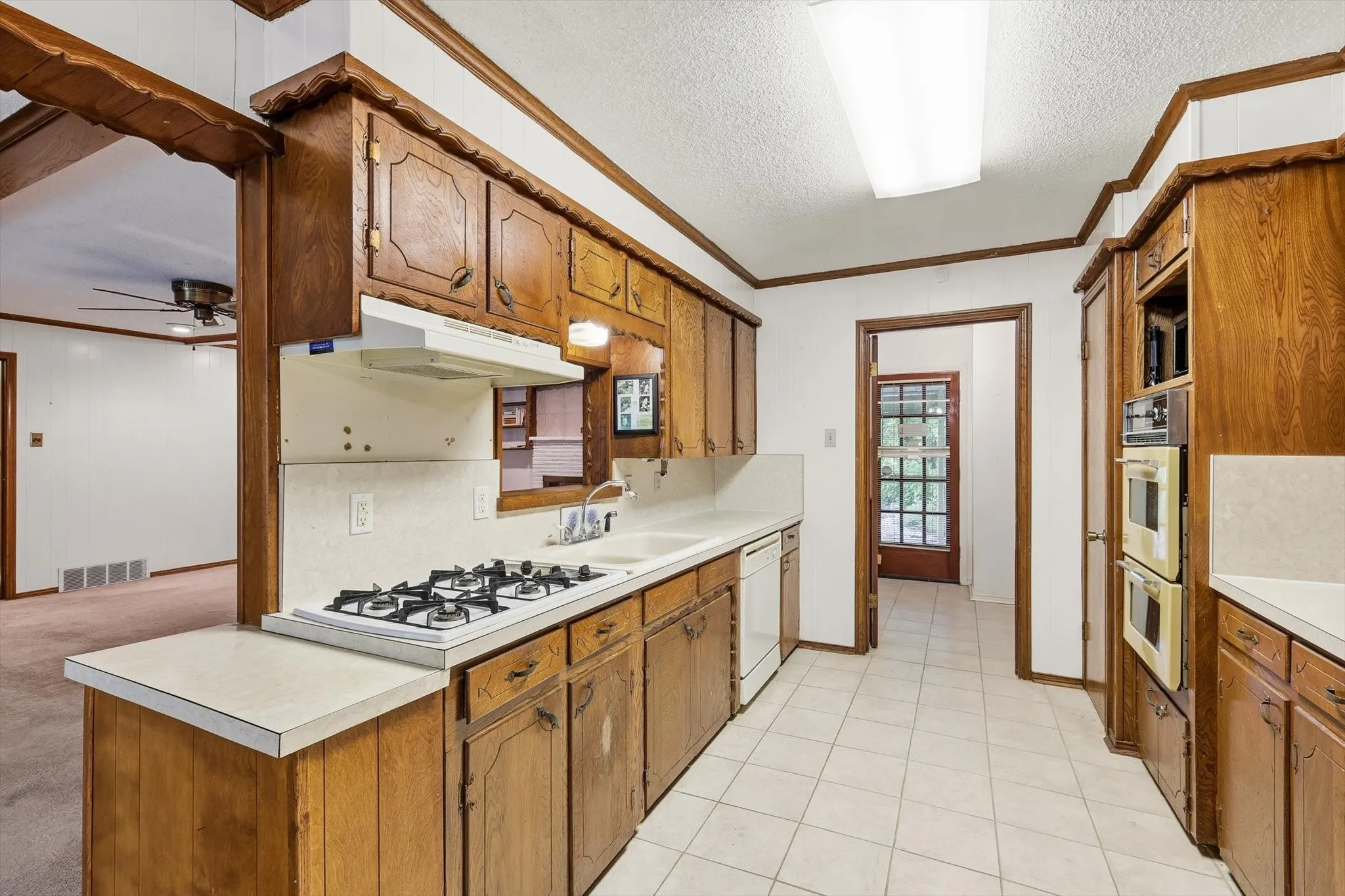 Kitchen featuring wood cabinetry, laminate countertops, a gas cooktop, double wall ovens, and tile flooring
