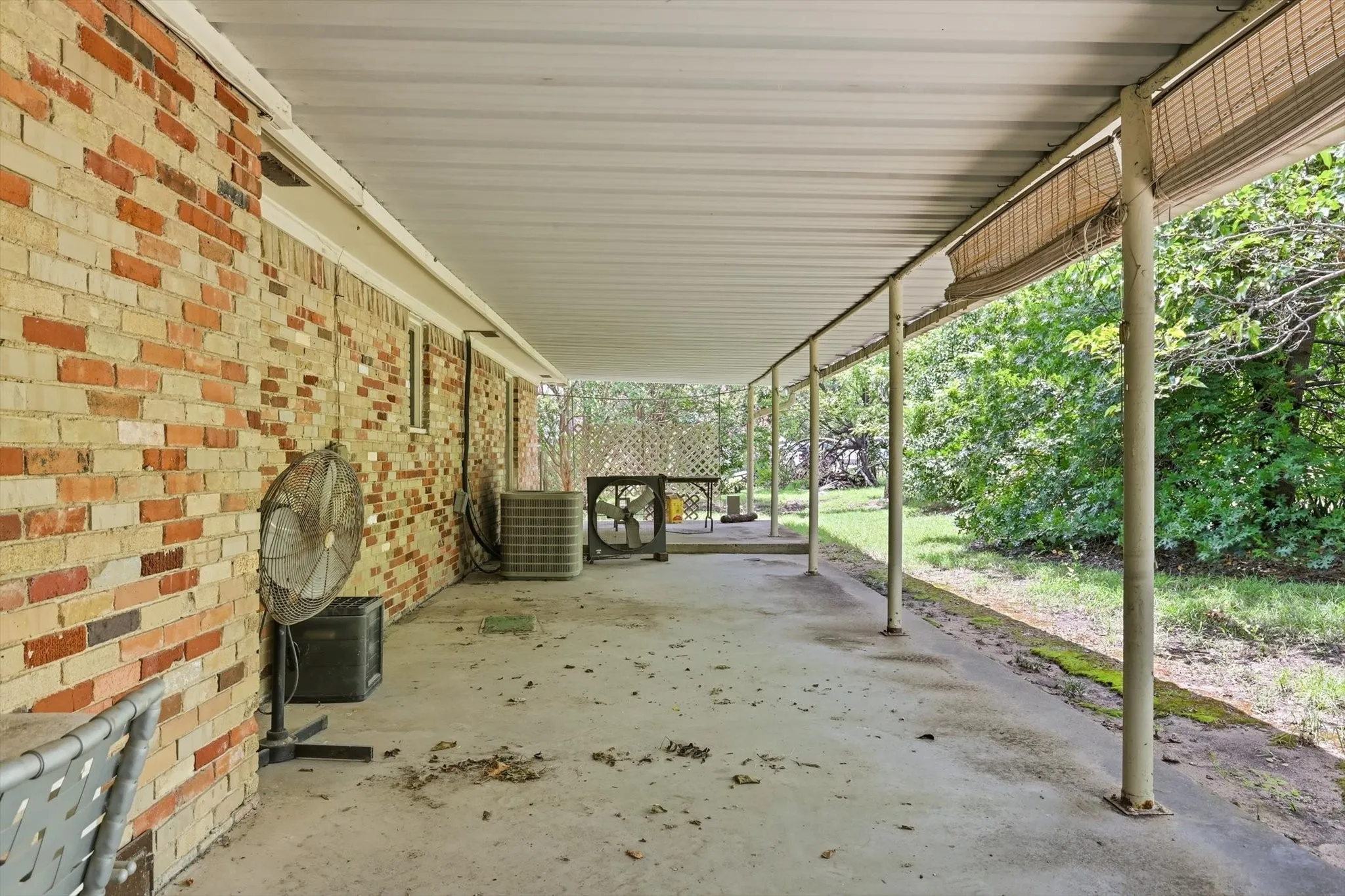 Expansive covered patio featuring a concrete slab, brick exterior wall, and metal support posts