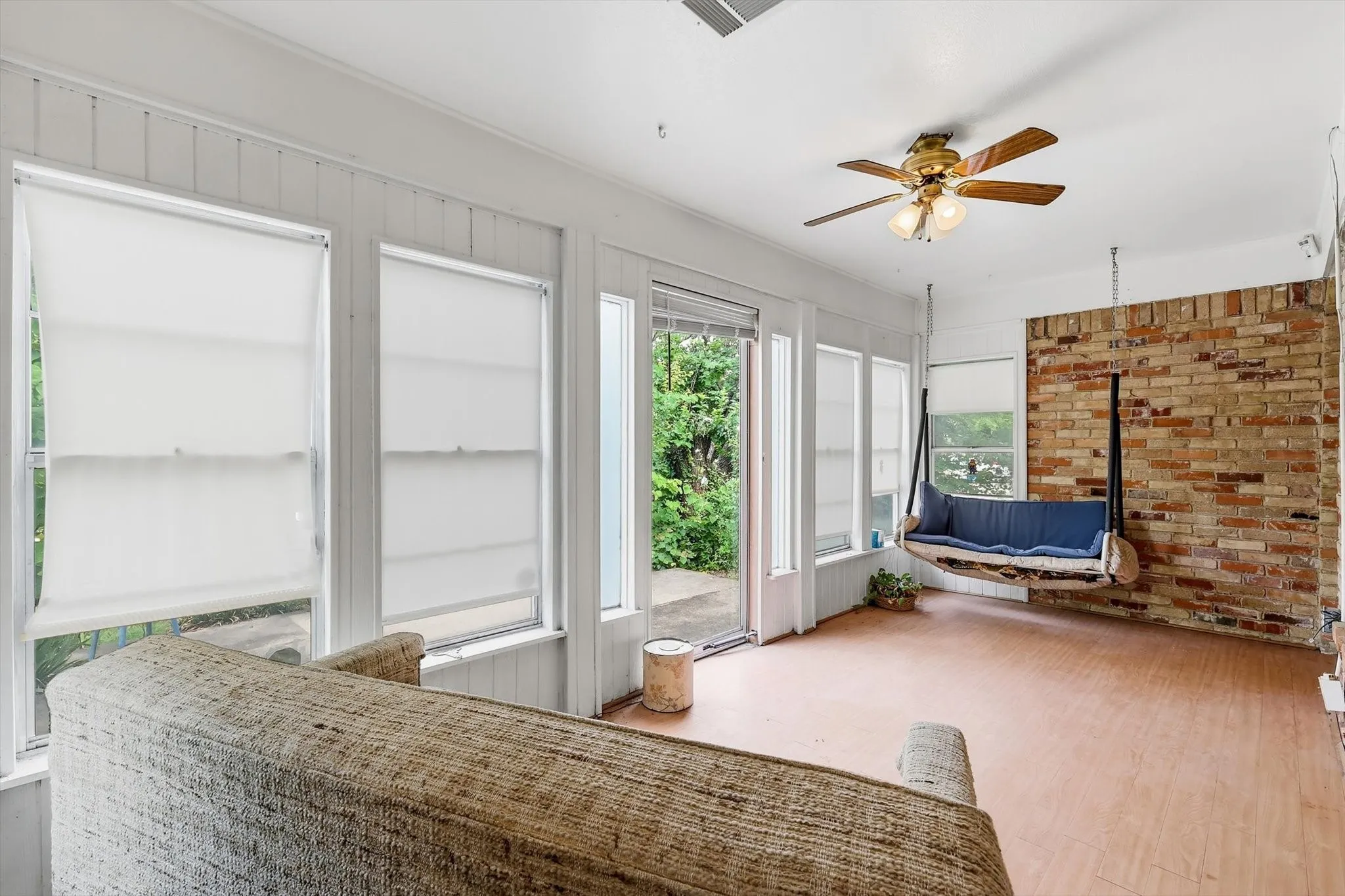 Sunroom featuring wood-finish flooring, a full brick accent wall, white paneling, multiple windows with roller shades, and an exterior door