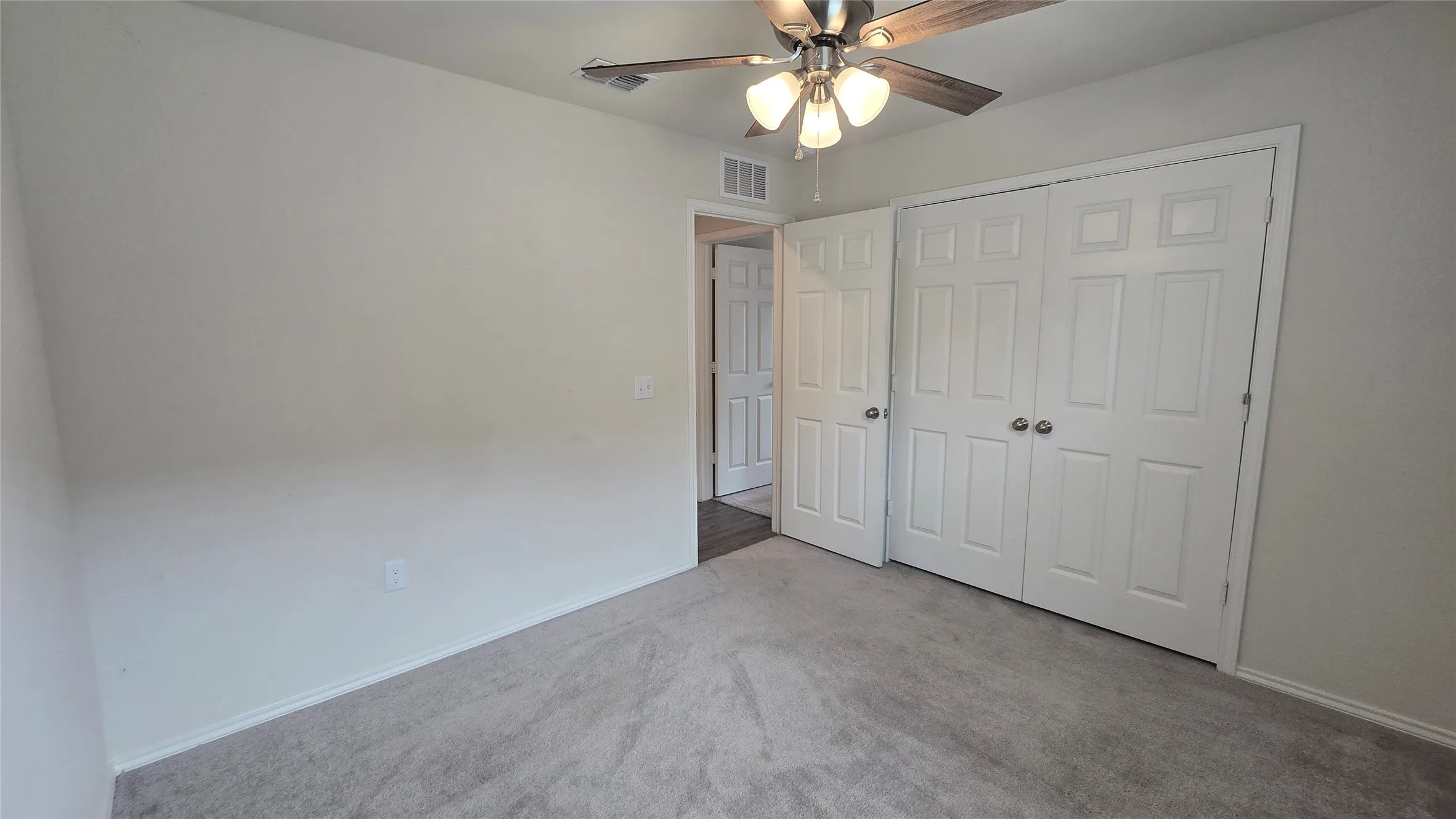 Carpeted room featuring a ceiling fan with light fixture, white interior doors, and neutral wall tones