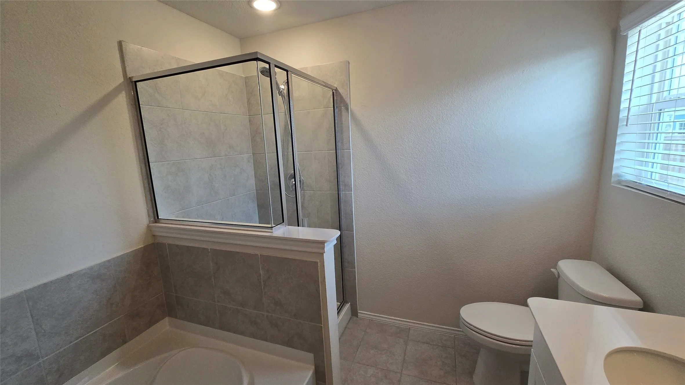 Bathroom featuring a glass-enclosed shower, tiled half-wall, and a window with blinds
