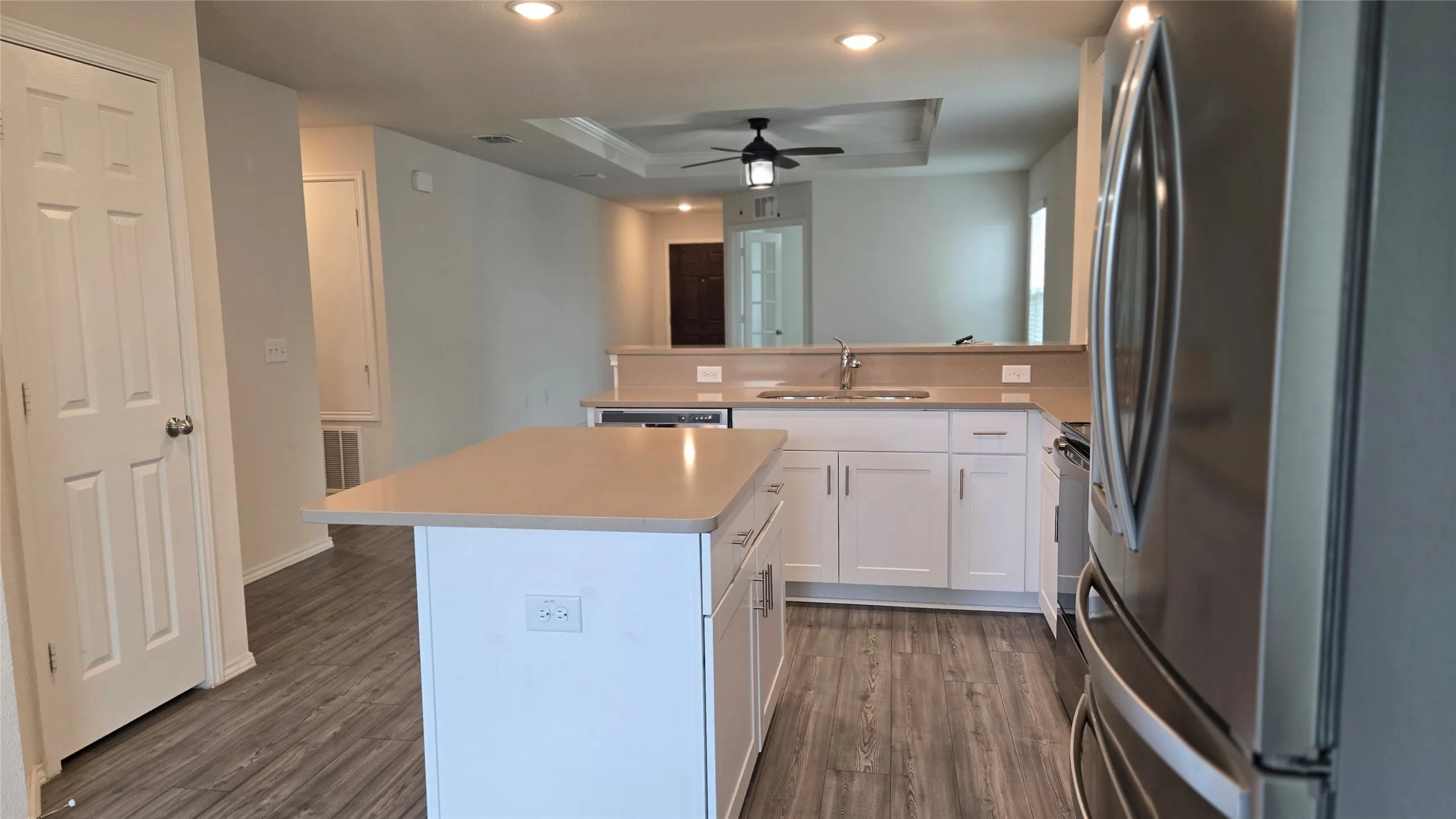 Modern kitchen featuring white cabinetry, light countertops, wood-finish flooring, a stainless steel refrigerator, and recessed lighting