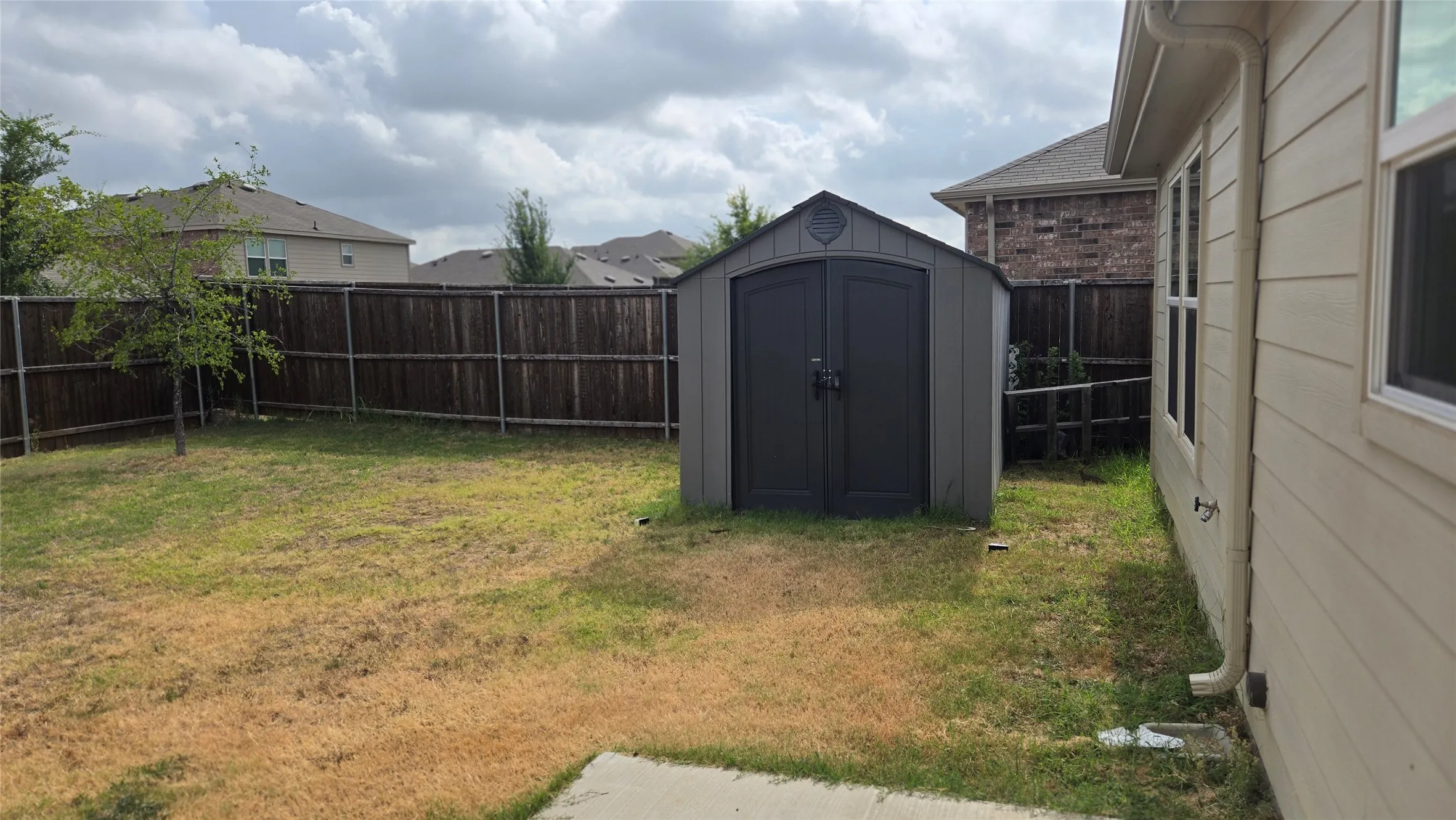 Spacious backyard featuring a storage shed with double doors, wood privacy fencing, a small tree, and a concrete patio section