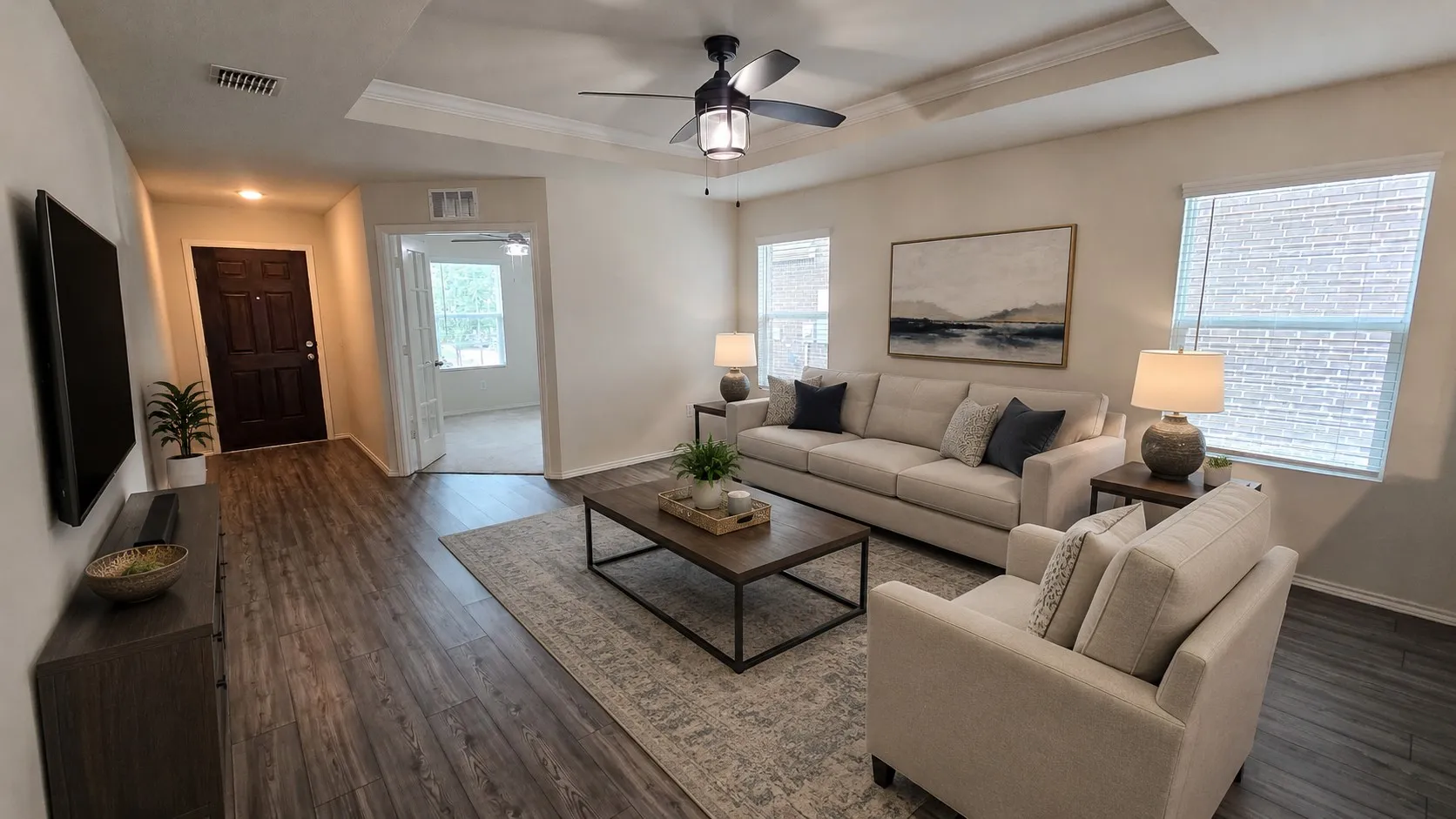 Virtual furnishings. Expansive living area featuring wood-finish flooring, a tray ceiling with a built-in fan, and multiple windows