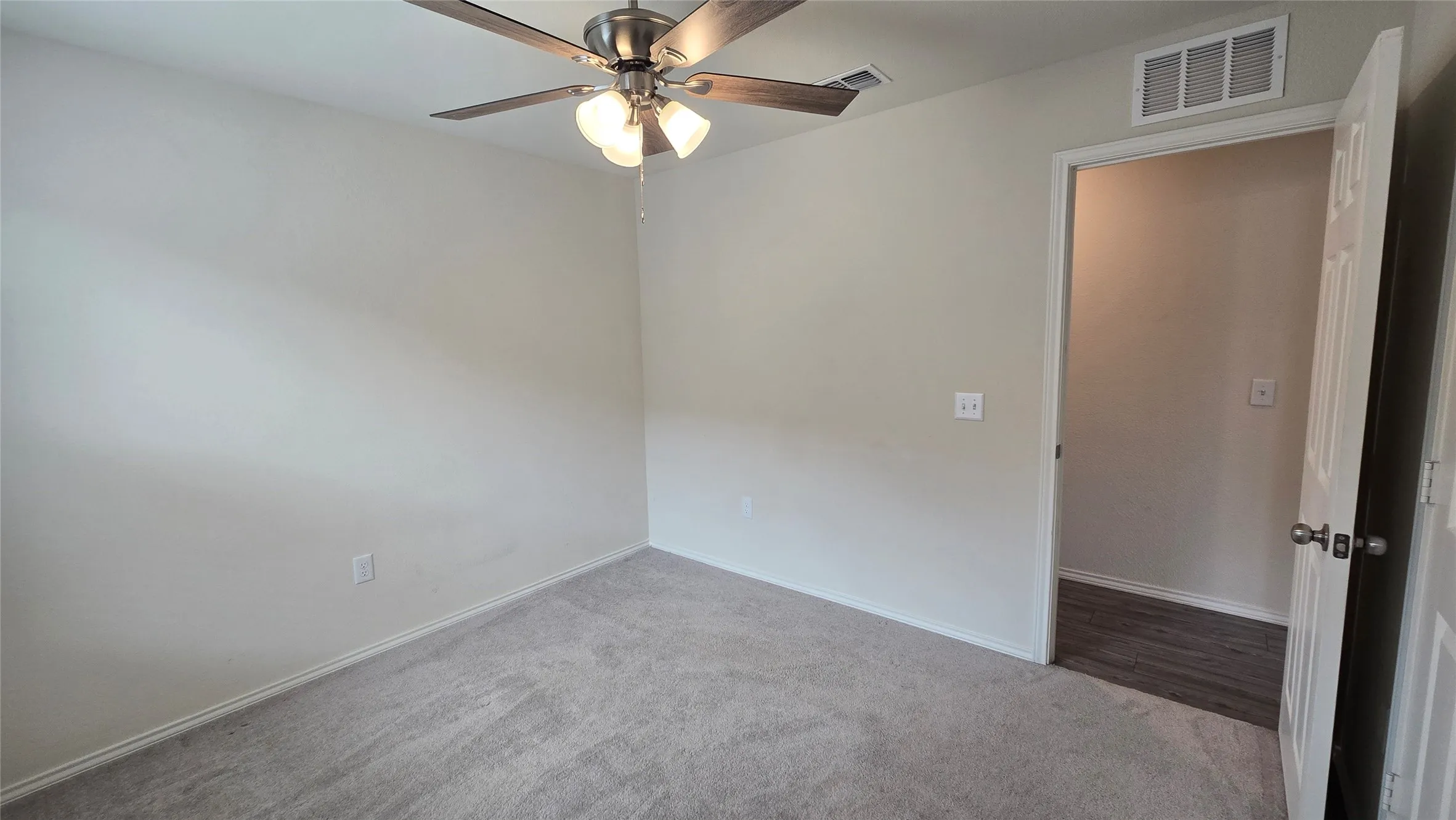Neutral wall paint and grey carpeting define this room, featuring a ceiling fan with light fixture