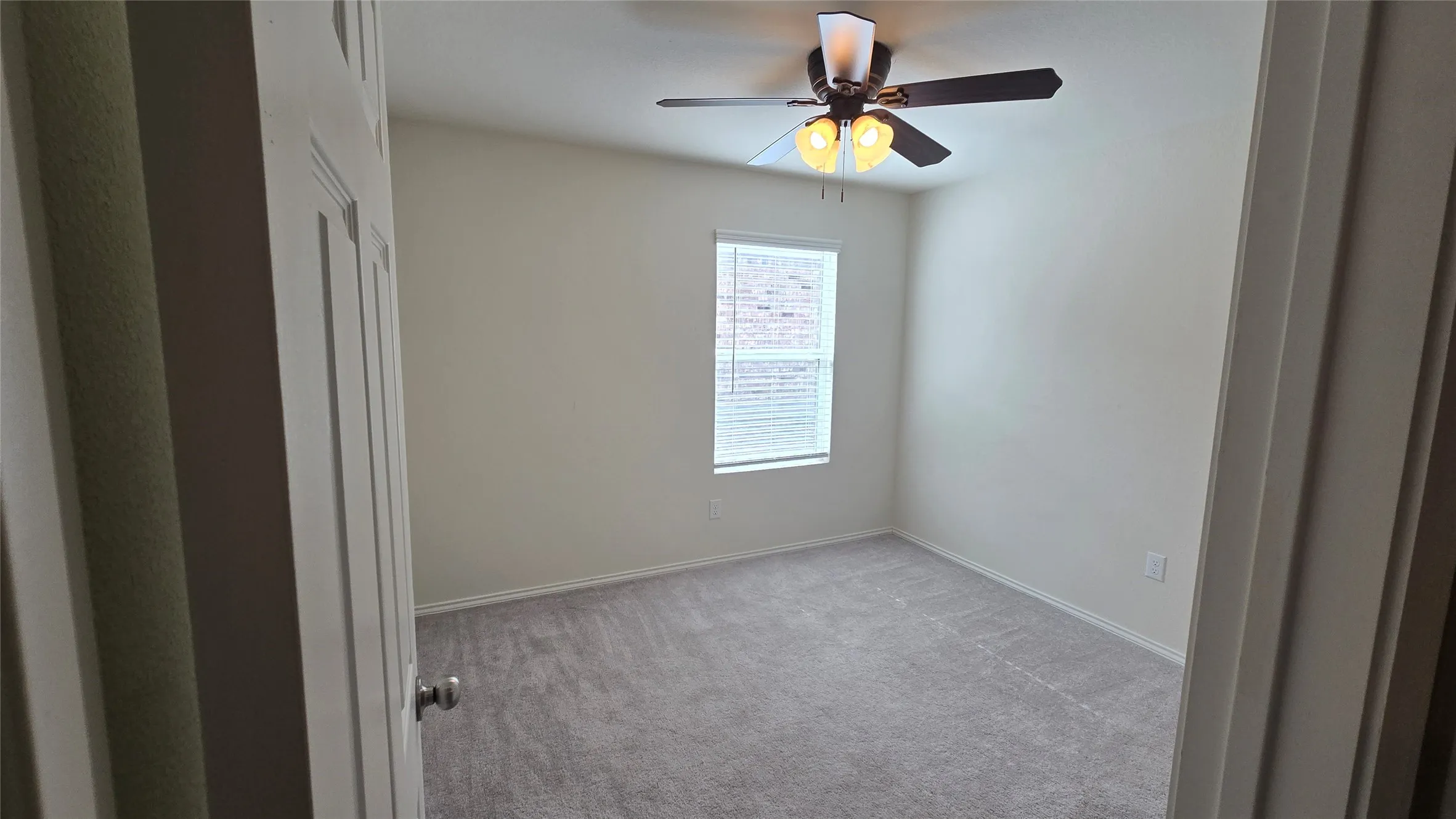Interior room featuring light gray carpet, a single window with blinds, and a ceiling fan with integrated lighting