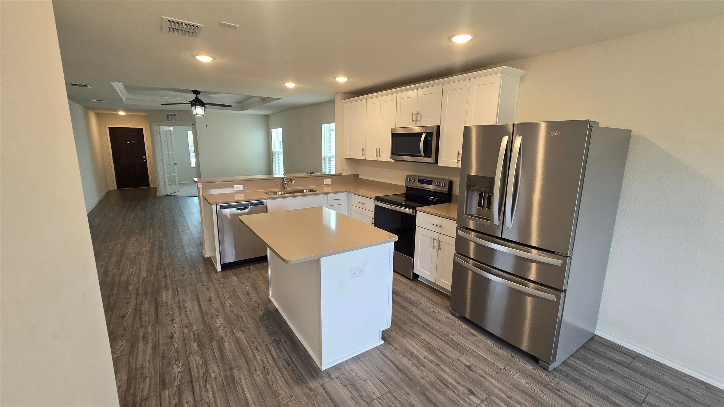 Open-concept kitchen featuring an island, white cabinetry, stainless steel appliances, and wood-finish flooring
