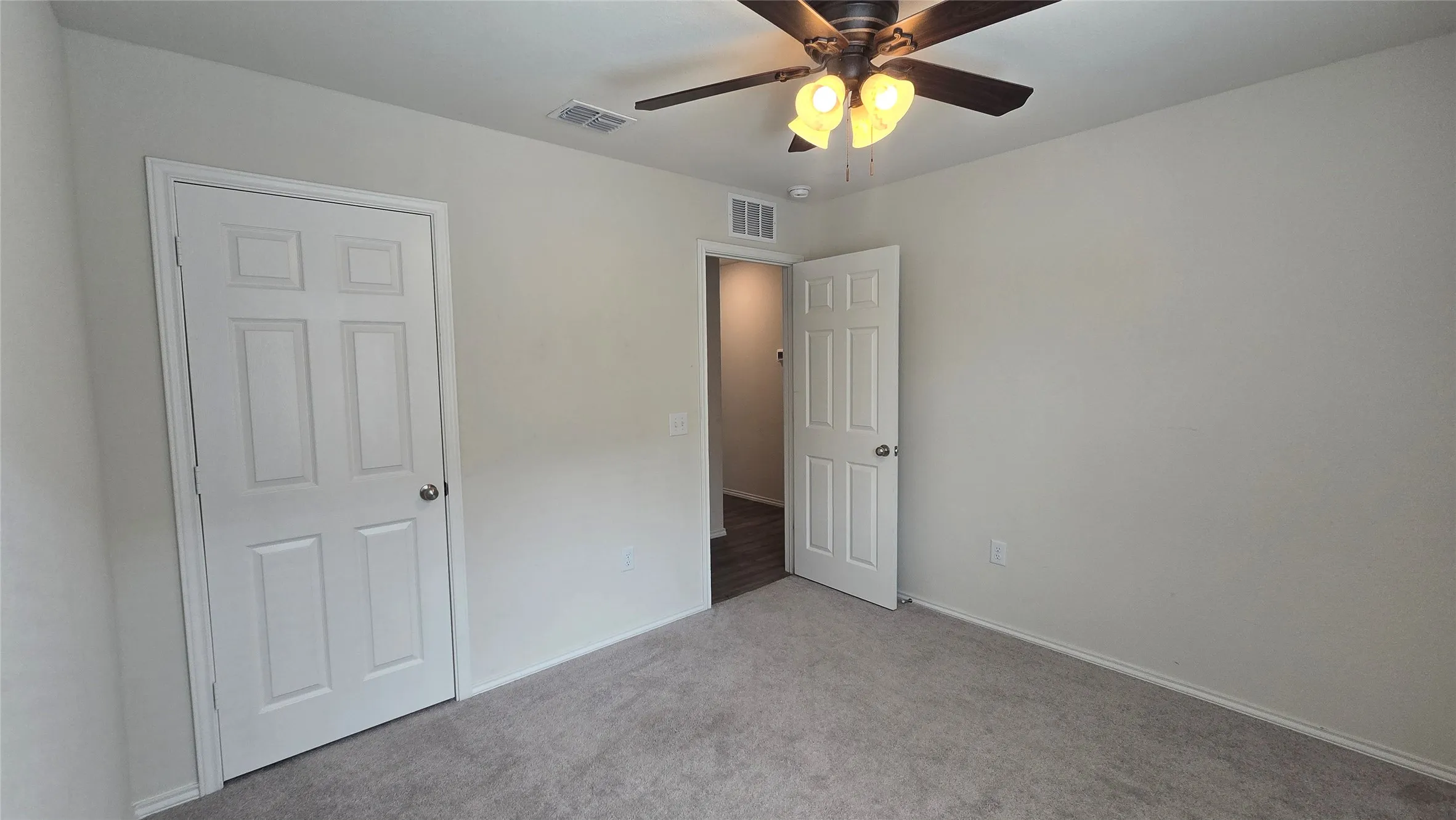 Carpeted room featuring a ceiling fan with light fixture, neutral wall paint, and white paneled doors