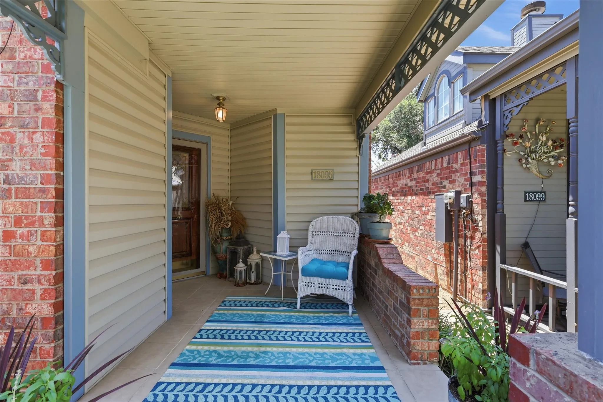 Covered porch entrance featuring a wooden door with glass pane, vinyl siding, brick accents, and a built-in overhead light fixture