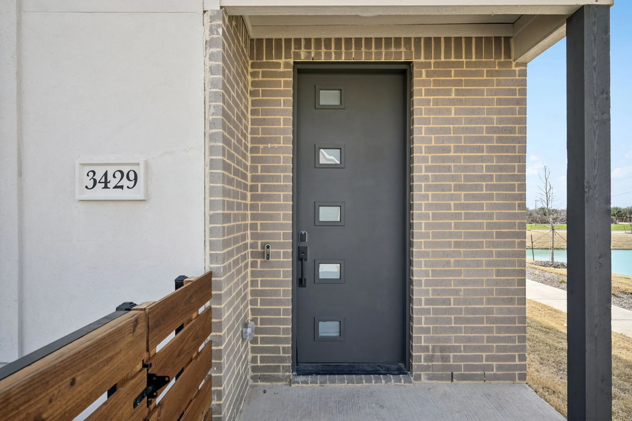 Modern front entry featuring a dark grey door with square lites, light brown brick facade, and a covered porch