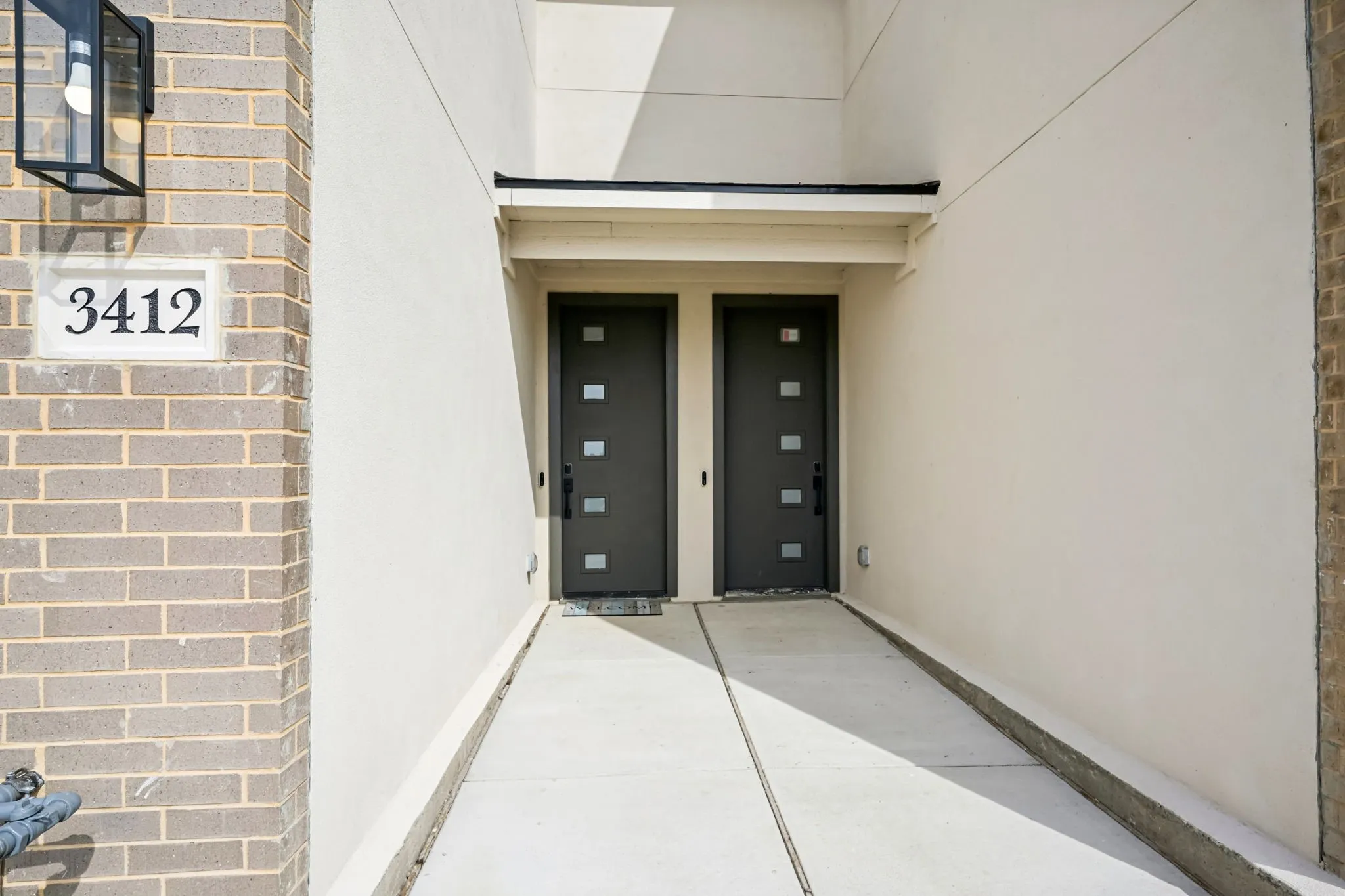 Modern exterior featuring light brick accents, stucco siding, dual entry doors with square window panels, and a concrete walkway