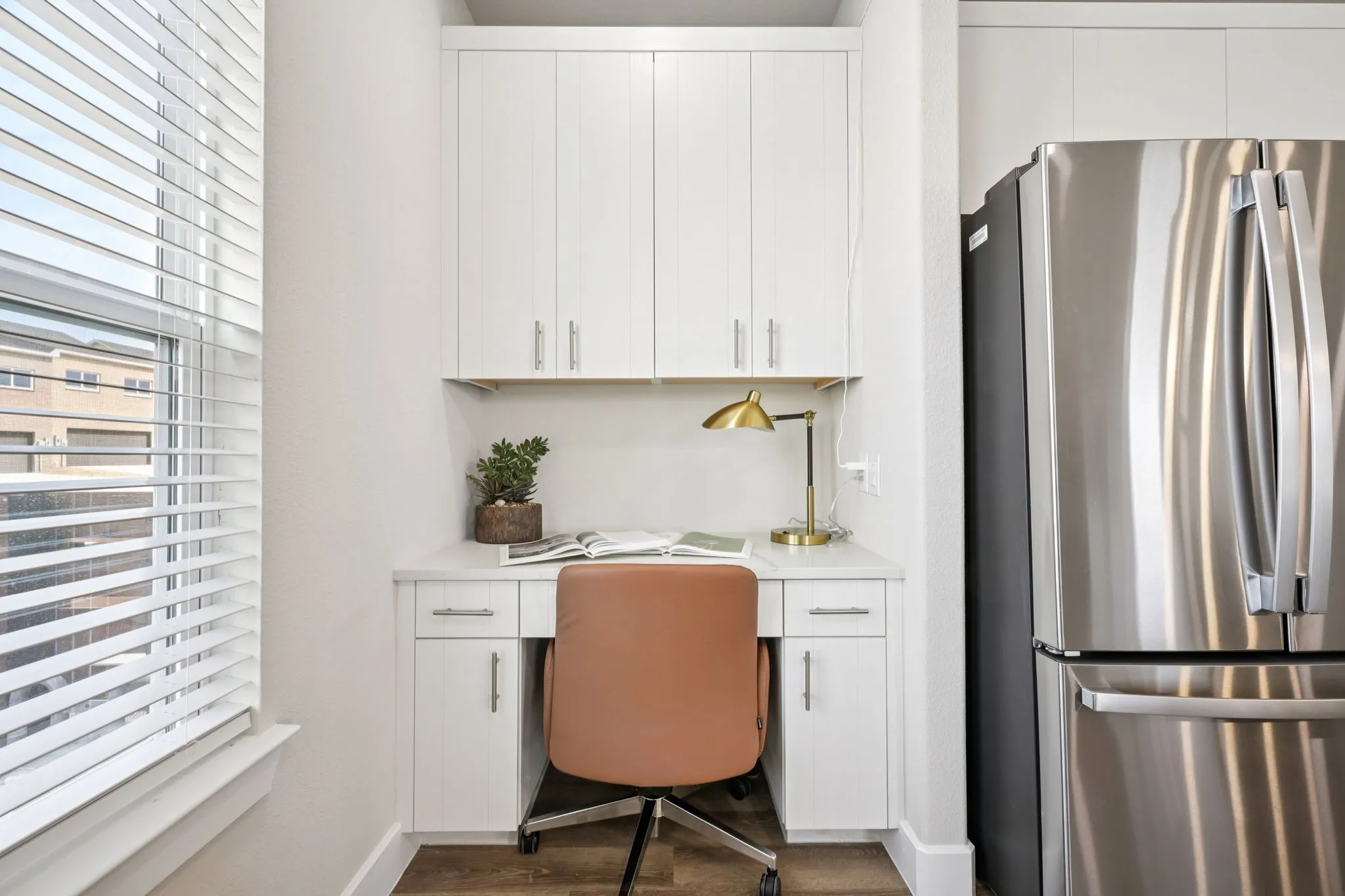 Built-in desk area featuring white cabinetry, a light-toned countertop, and wood-finish flooring