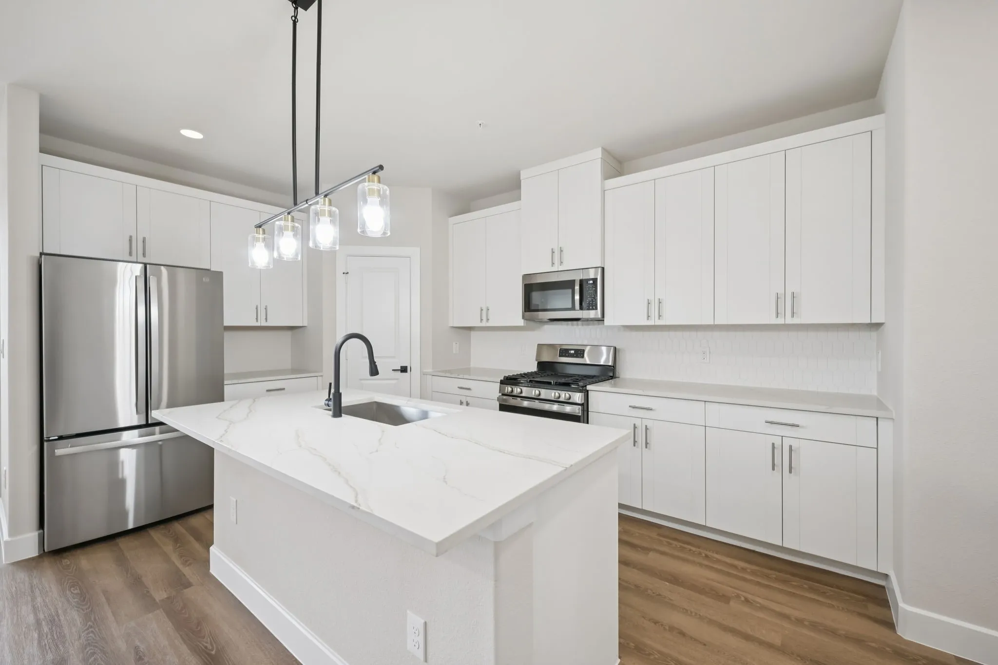 Modern kitchen featuring an expansive island with a waterfall countertop, undermount sink, and matte black faucet