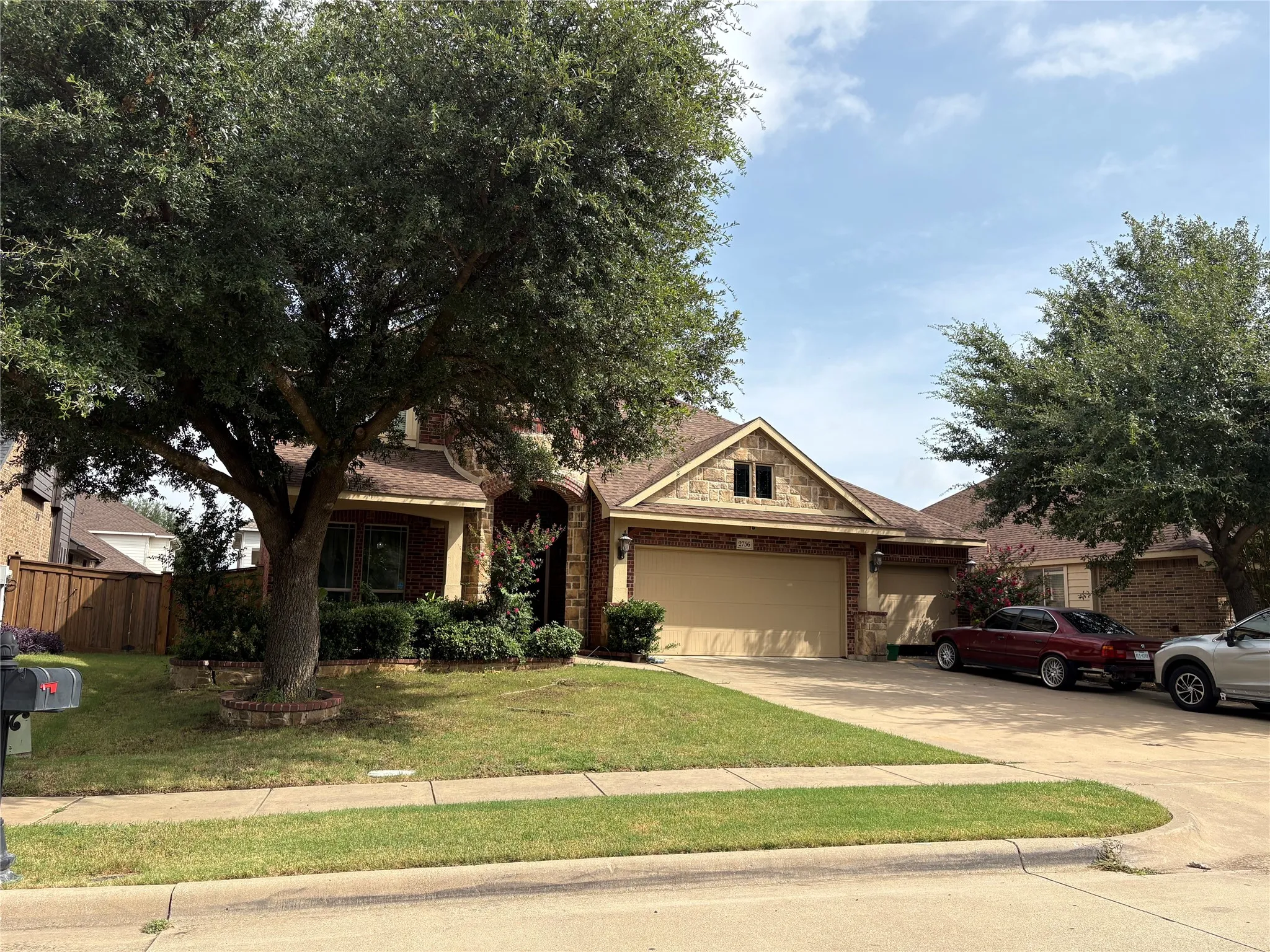 Traditional-style residence featuring a brick and stone facade, mature trees, and a 3-car garage