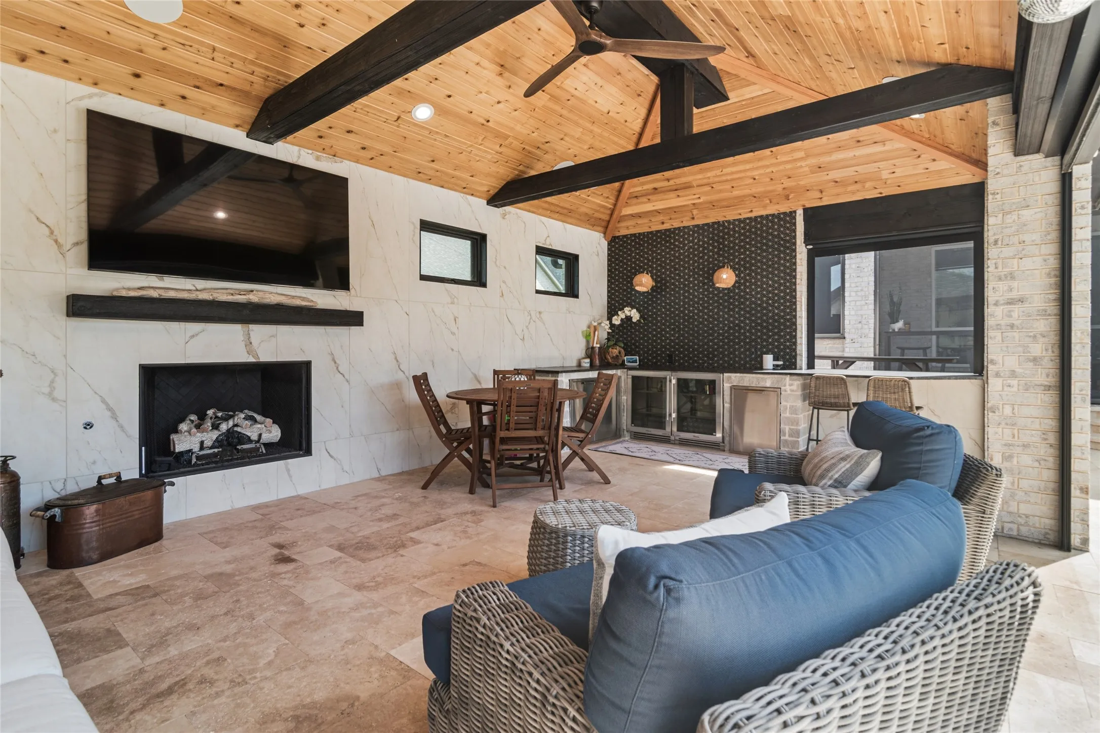 Inside of the pool house, fireplace, vaulted cedar ceiling, travertine flooring, tiled wall with transom windows. L shaped counter top for serving with counter for bar seating. Custom tile above counter.