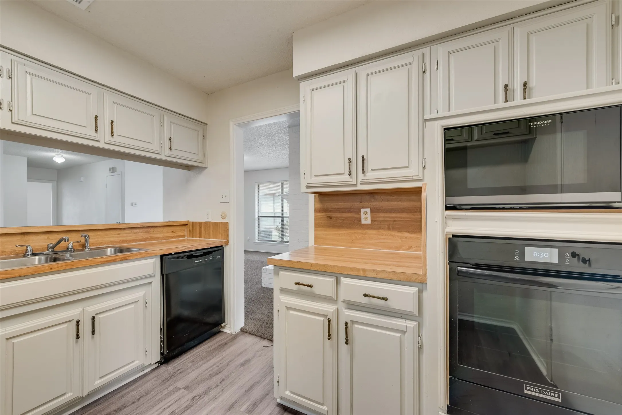 Kitchen featuring wood-finish countertops, light-toned cabinetry with dark hardware, a built-in microwave, and a black oven