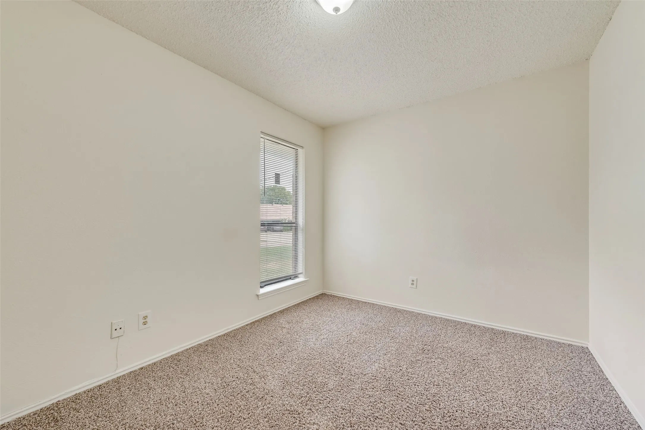 Neutral tone walls with a textured ceiling, a single window, and carpeted flooring