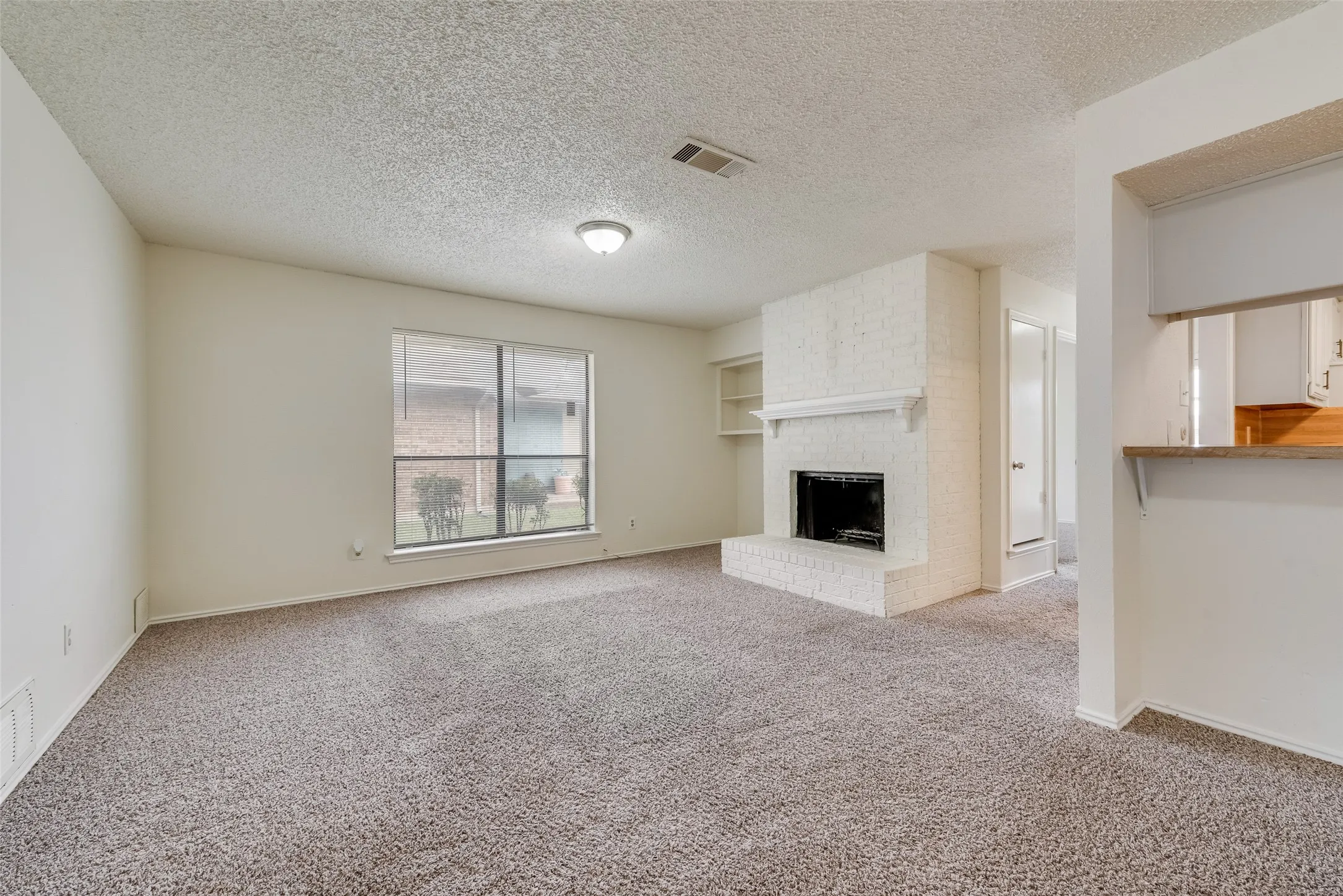 Living area featuring a painted brick fireplace, a built-in shelf, and a pass-through window with a wood-finish bar top