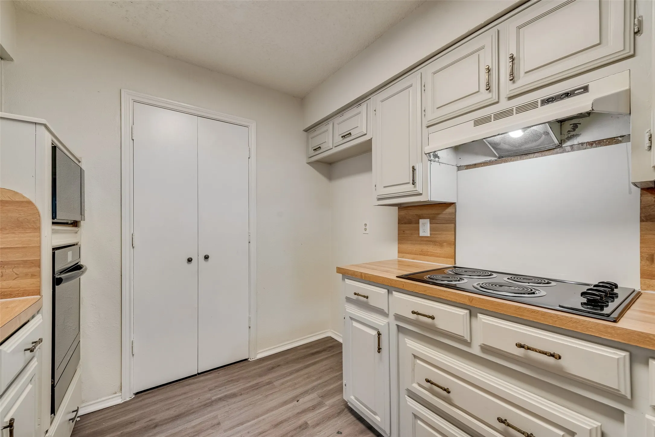 Kitchen featuring wood-finish countertops, white cabinetry with bronze hardware, and a built-in electric cooktop