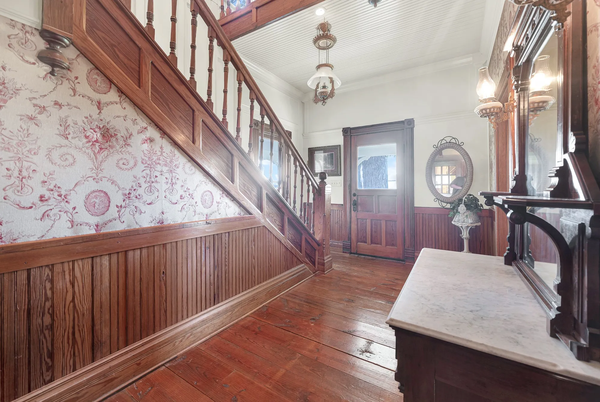 Original fabric wall coverings, handcrafted millwork, and an adjustable pull-down pendant light reflect the remarkable craftsmanship preserved throughout the foyer. Stepping inside feels like discovering a home where history has been thoughtfully cared for.