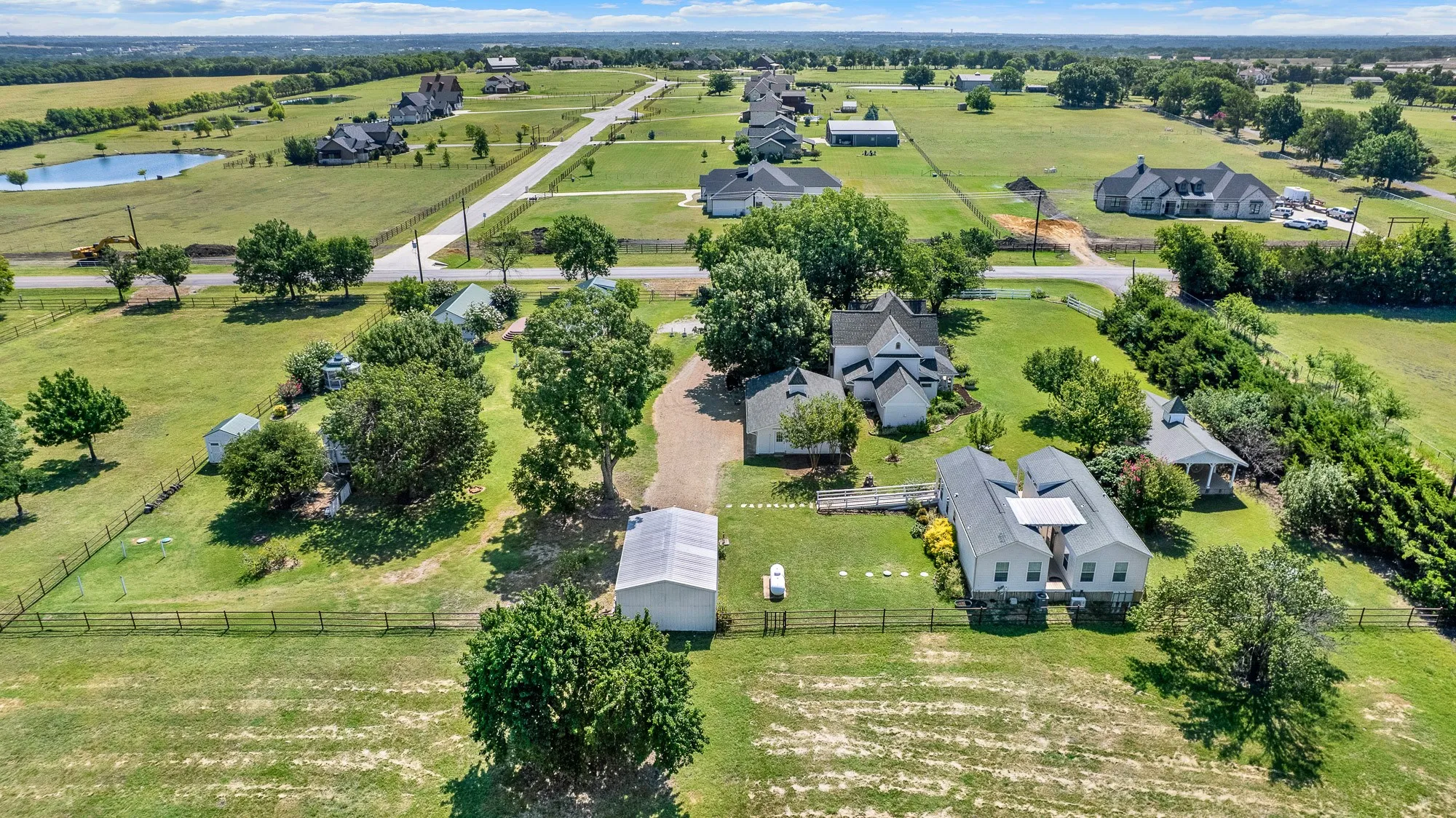 This aerial showcases the timeless architecture of the beautifully restored historic residence, nestled beneath a canopy of mature trees. The wraparound porch, thoughtfully landscaped grounds, and seamless blend of original character with modern updates make this home the centerpiece of the estate. Positioned on a spacious corner lot in an area of newer luxury acreage properties, it offers both historic charm and enduring value.