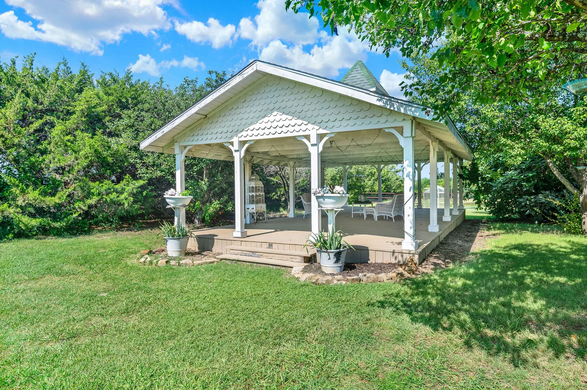 The expansive covered pavilion is an inviting gathering space designed for entertaining, celebrations, or simply enjoying the peaceful country setting. With its open-air design, exposed timber framing, and generous footprint, it comfortably accommodates everything from family barbecues to special events while overlooking the beautifully maintained grounds.
