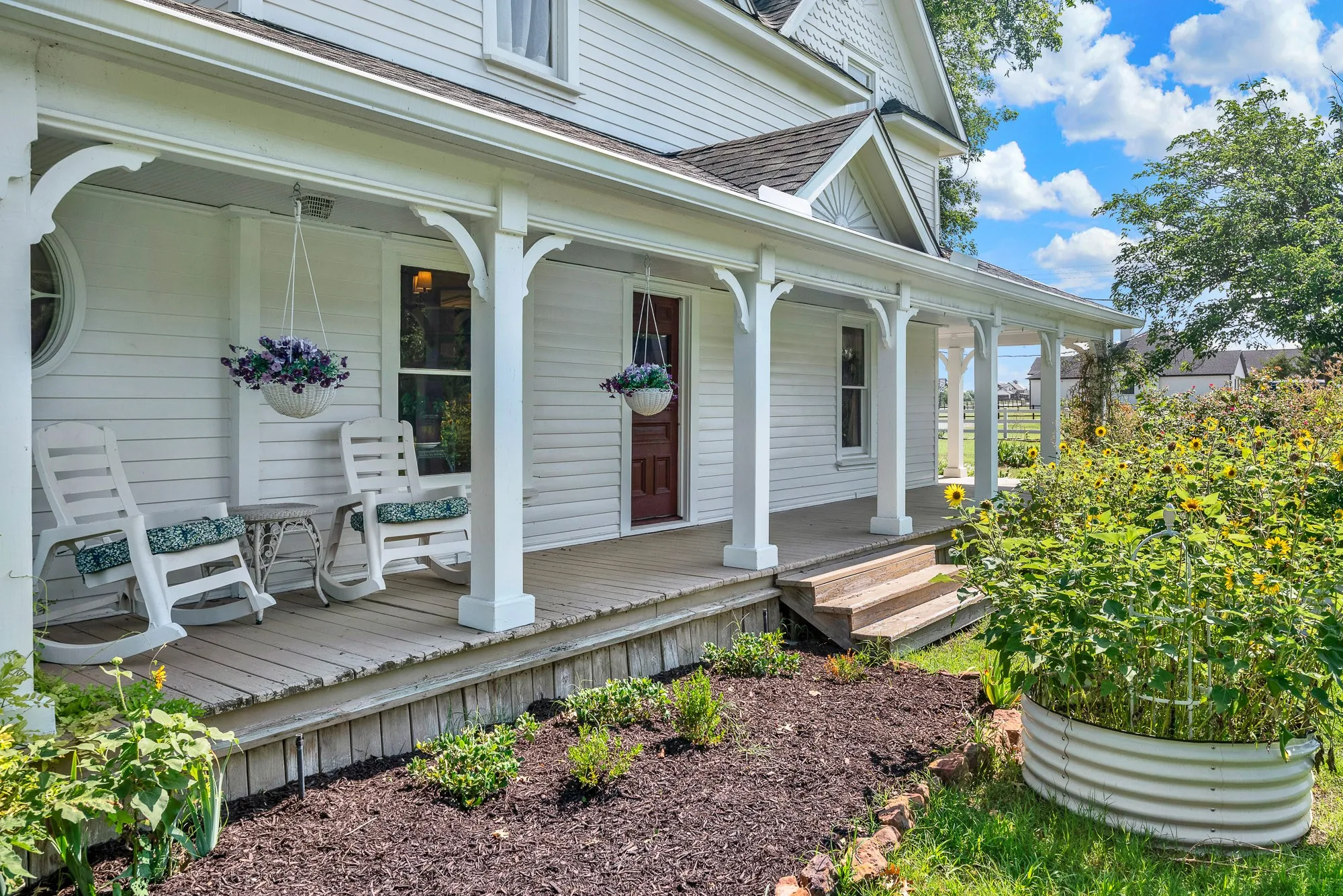 The wide wraparound porch, framed by classic brackets and surrounded by blooming gardens, creates a graceful transition between the home and its scenic surroundings. It's the kind of place where mornings begin in a rocking chair with coffee and evenings end watching the sunset over the pasture.