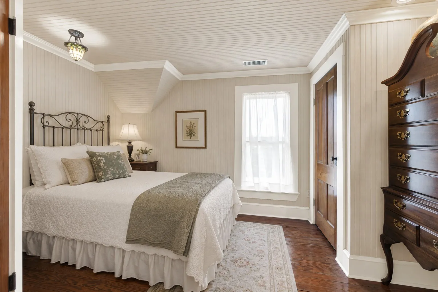 Original hardwood floors and soft natural light create a bright, welcoming retreat, while the angled ceiling adds architectural character without sacrificing usable space. It's an inviting room for guests or family to unwind, offering a peaceful place to relax after a day spent enjoying the property.