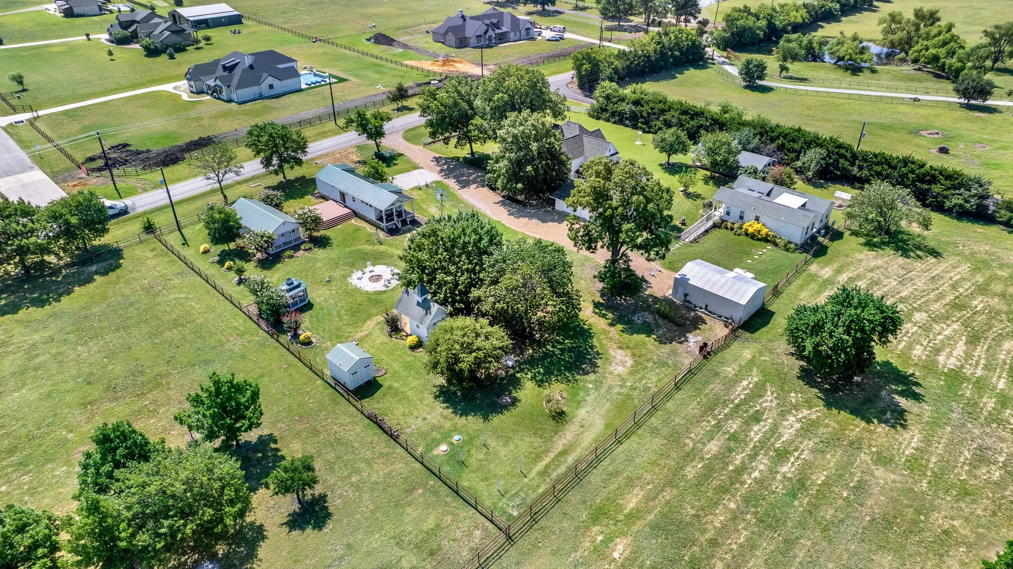 From this angle, the property's park-like setting truly shines. Mature trees, open green space, and well-planned improvements—including the rental cottages, gazebo, pavilion, and gathering areas—create a welcoming environment with room to relax and entertain. The estate enjoys the peaceful feel of country living while being surrounded by attractive newer custom homes on large acreage tracts.