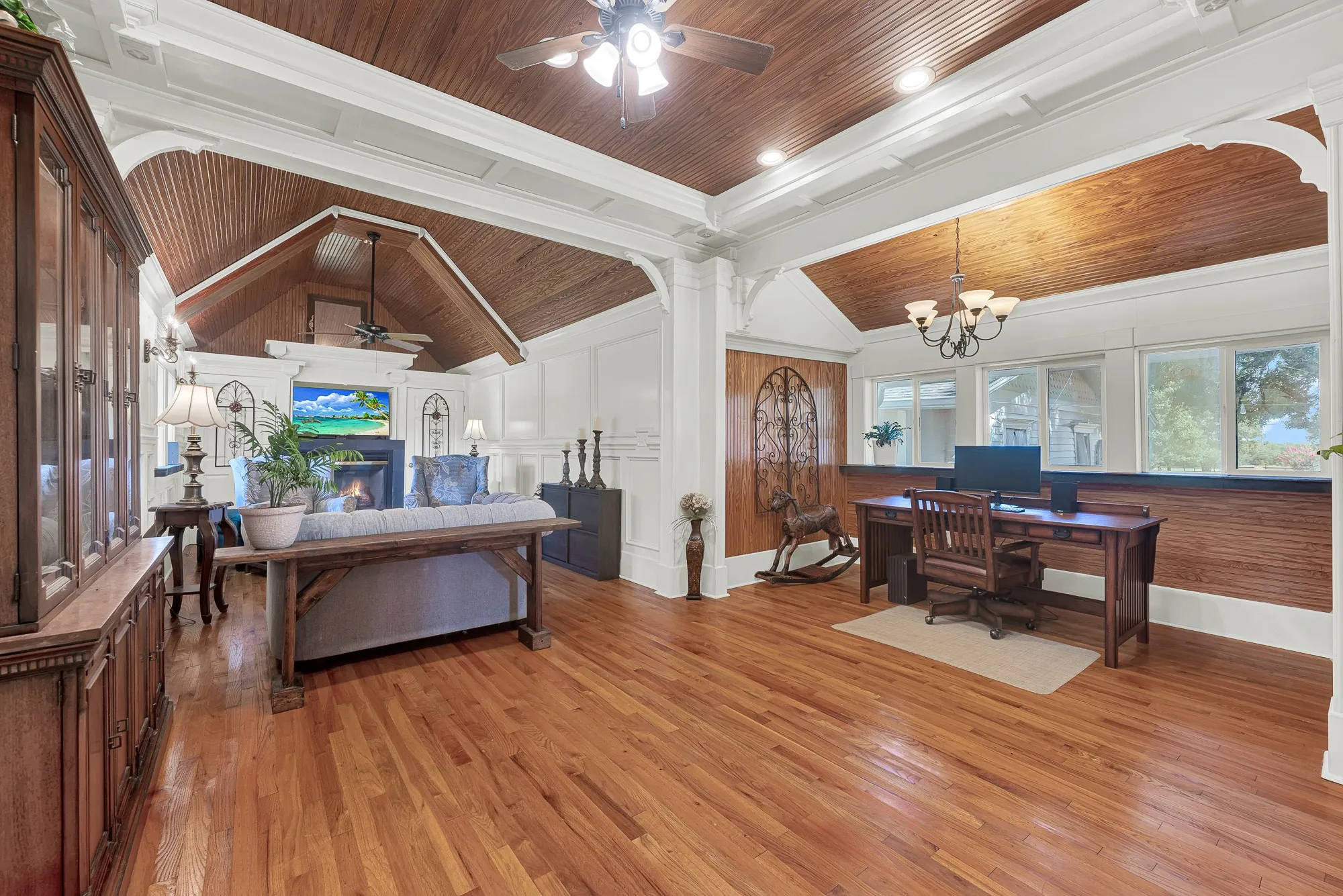 This expansive family room blends warmth and functionality with rich wood ceilings, original hardwood floors, elegant millwork, and a cozy fireplace. A dedicated office nook with built-in workspace overlooks the grounds, while abundant natural light and an open layout create an inviting space for everyday living, working from home, or entertaining.