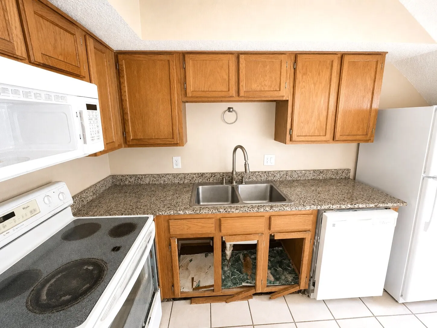 Kitchen featuring wood cabinetry, a dual basin sink with a gooseneck faucet, light-toned countertops, and a built-in microwave