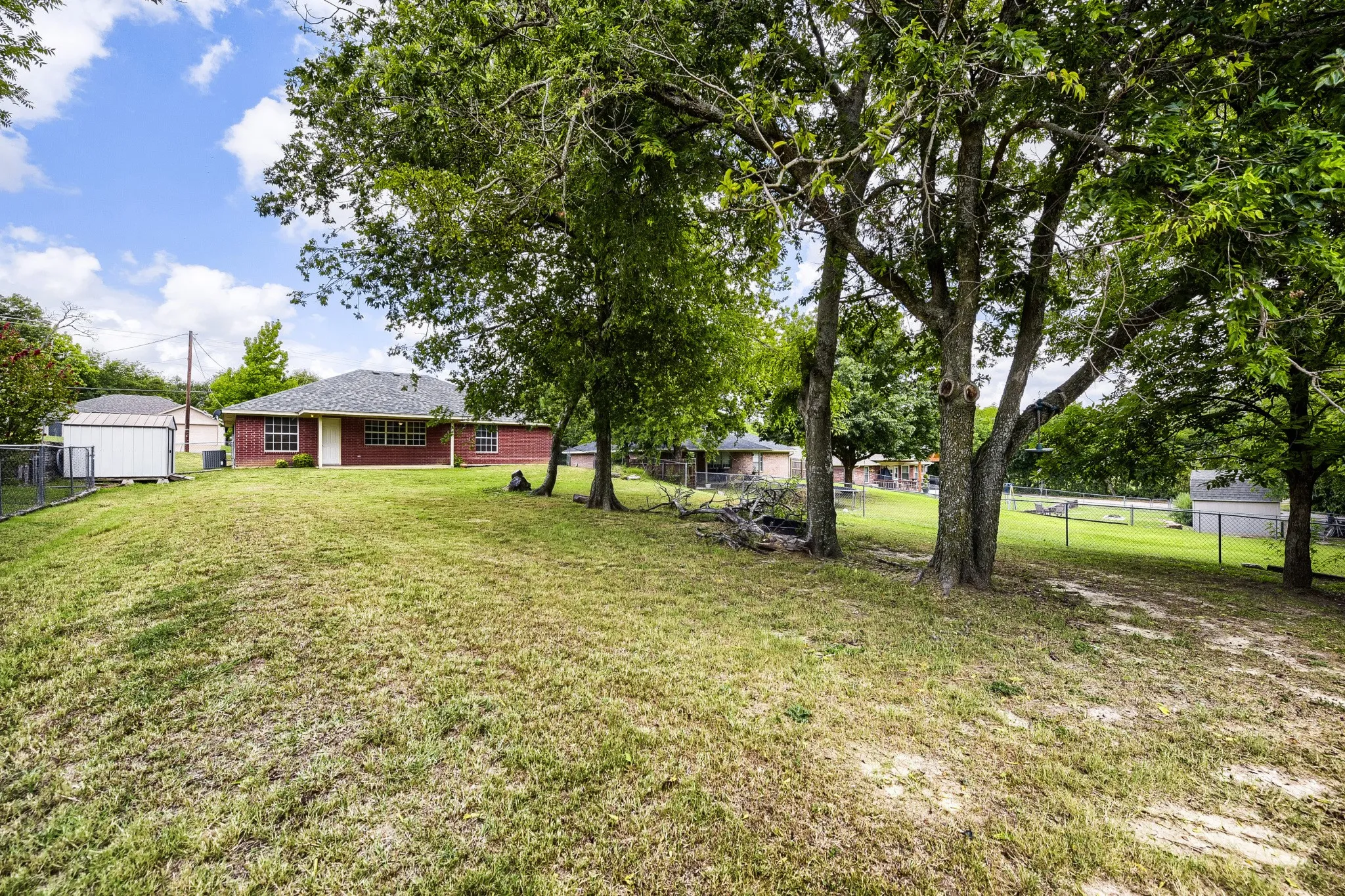 Expansive rear yard featuring mature trees and a sloped, grassy terrain